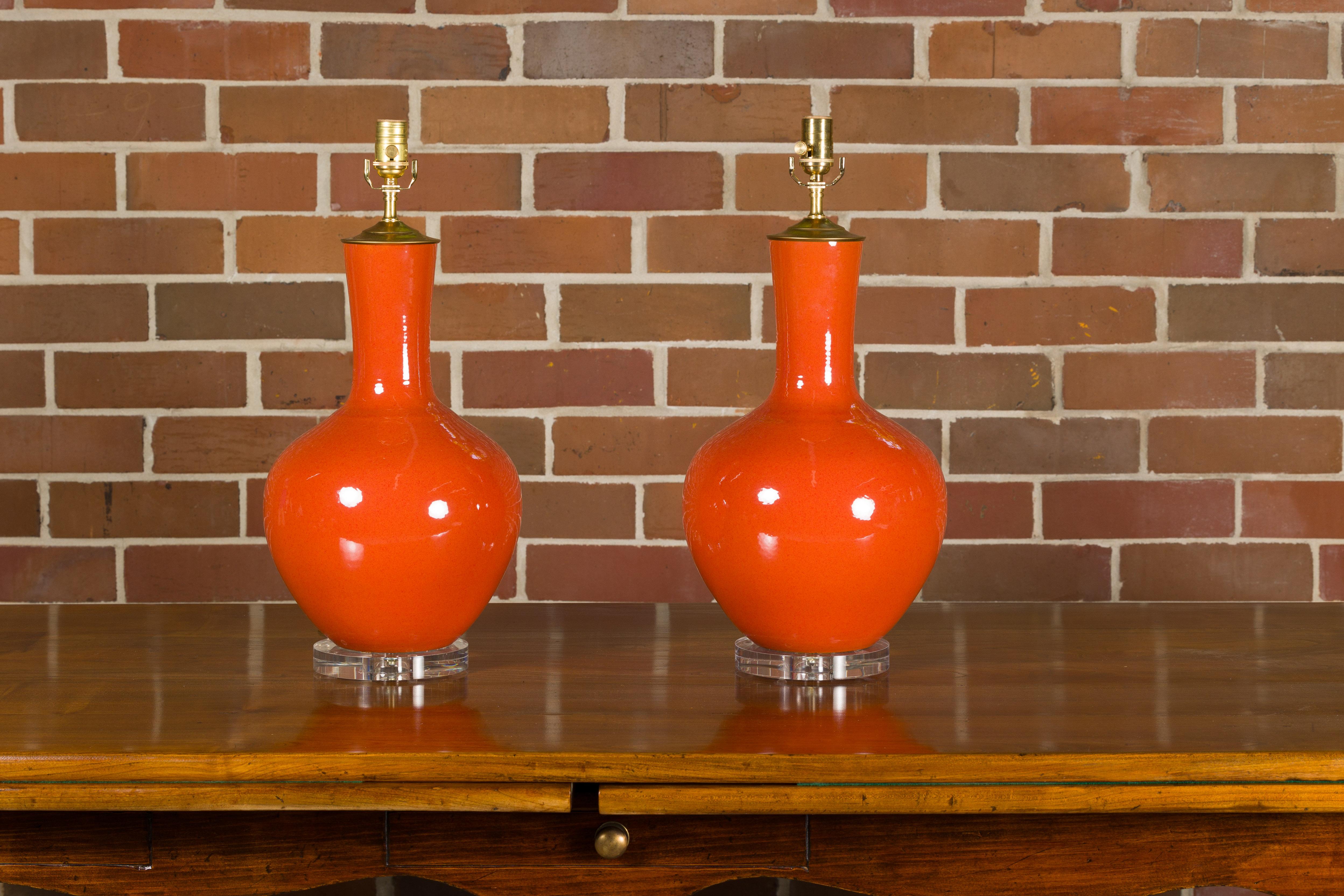 A pair of Asian burnt orange porcelain table lamps on circular lucite bases. This pair of Asian burnt orange porcelain table lamps, resting on sleek circular lucite bases, exudes a warm, vibrant charm, perfect for infusing a touch of the Orient into
