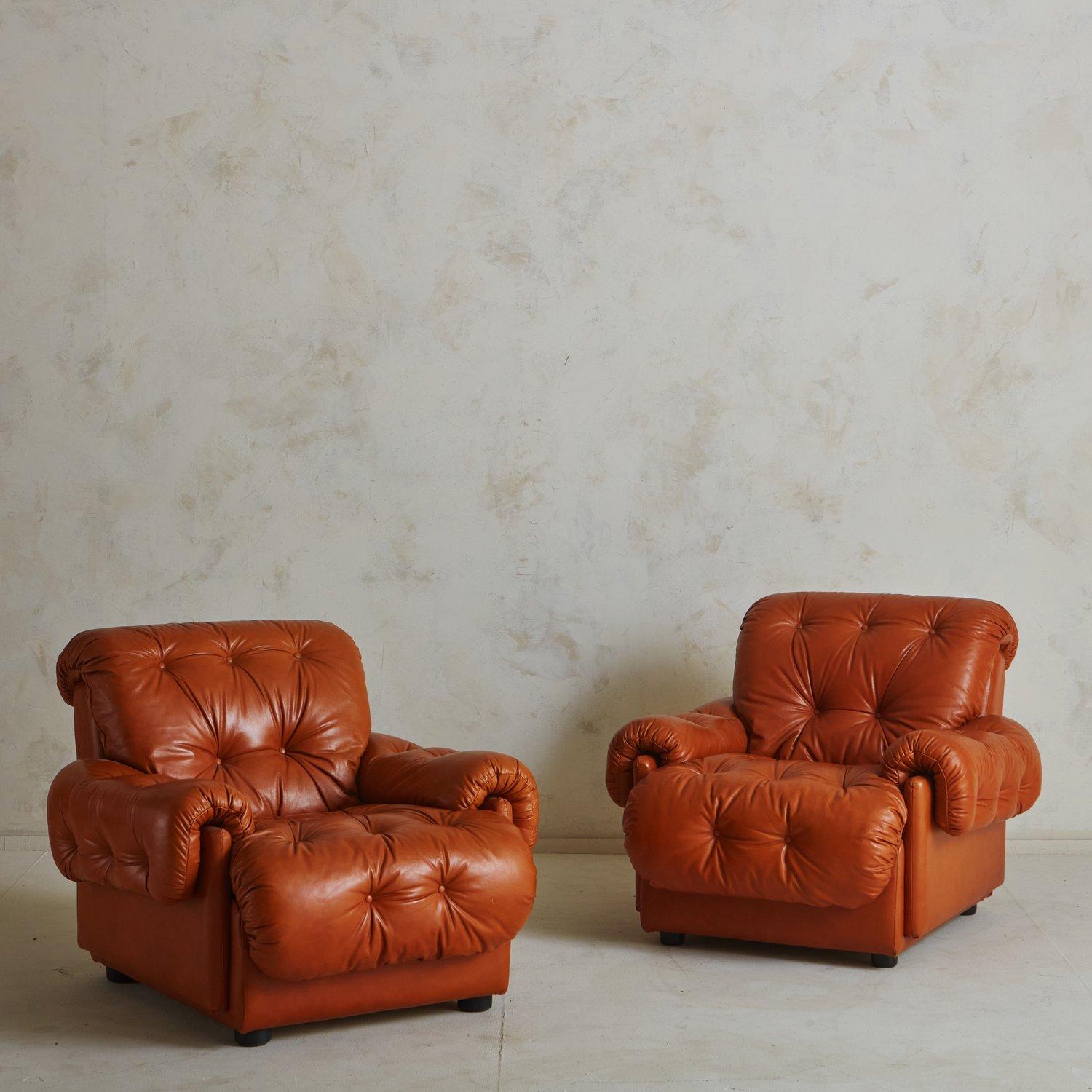 A handsome pair of 1960s Italian lounge chairs in a rich cognac leather. These stately chairs feature button tufted seat backs, cushions and arms, which drape beautifully over the angular frame. They have ruched detailing along the edges and stand