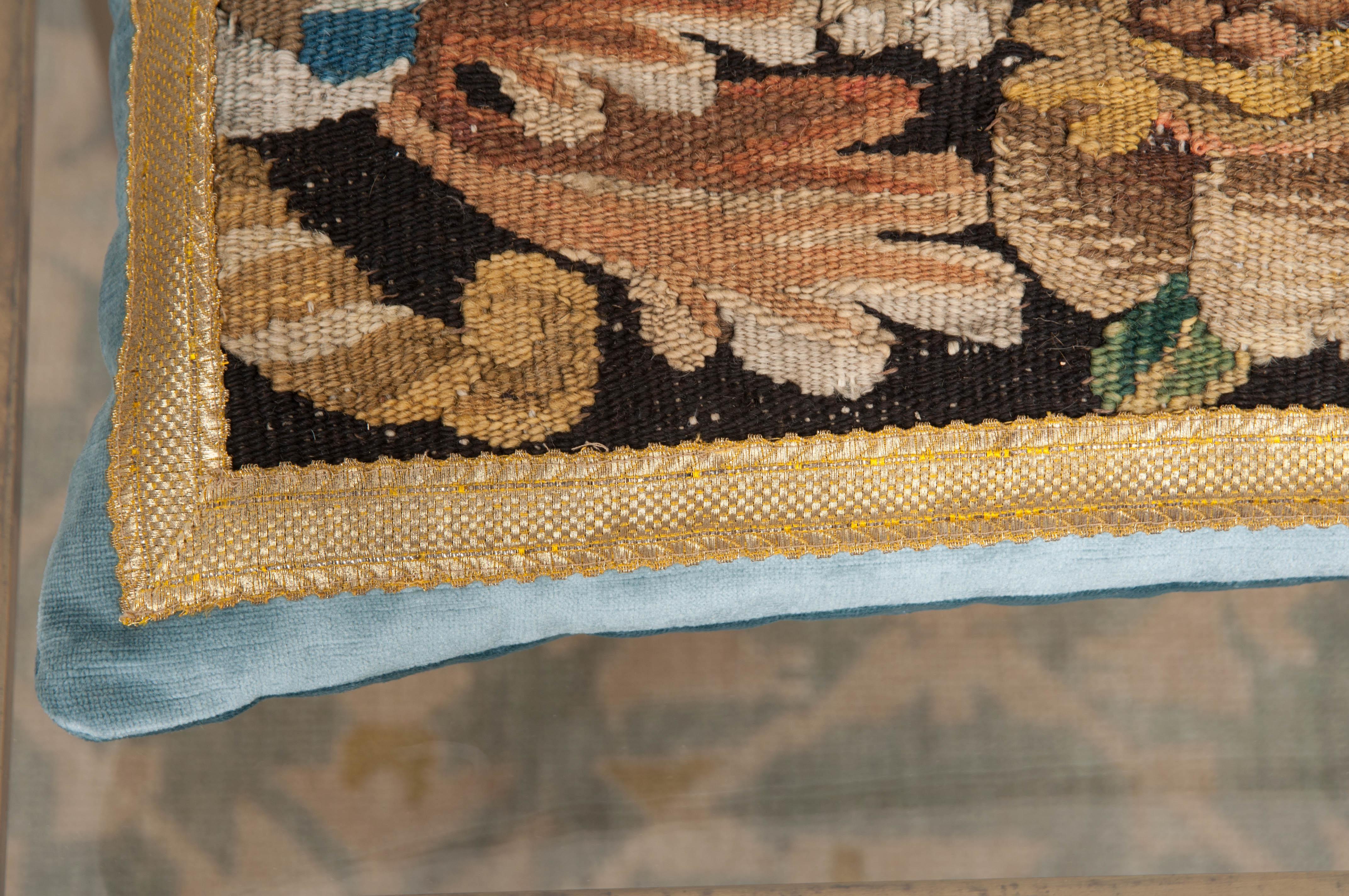 Antique tapestry fragment in shades of blue, green, gold, and khaki framed with antique silver metallic gallon on pale French blue velvet. Hand-trimmed with vintage silver-metallic cording which is knotted in the corners. Down-filled. Designed by