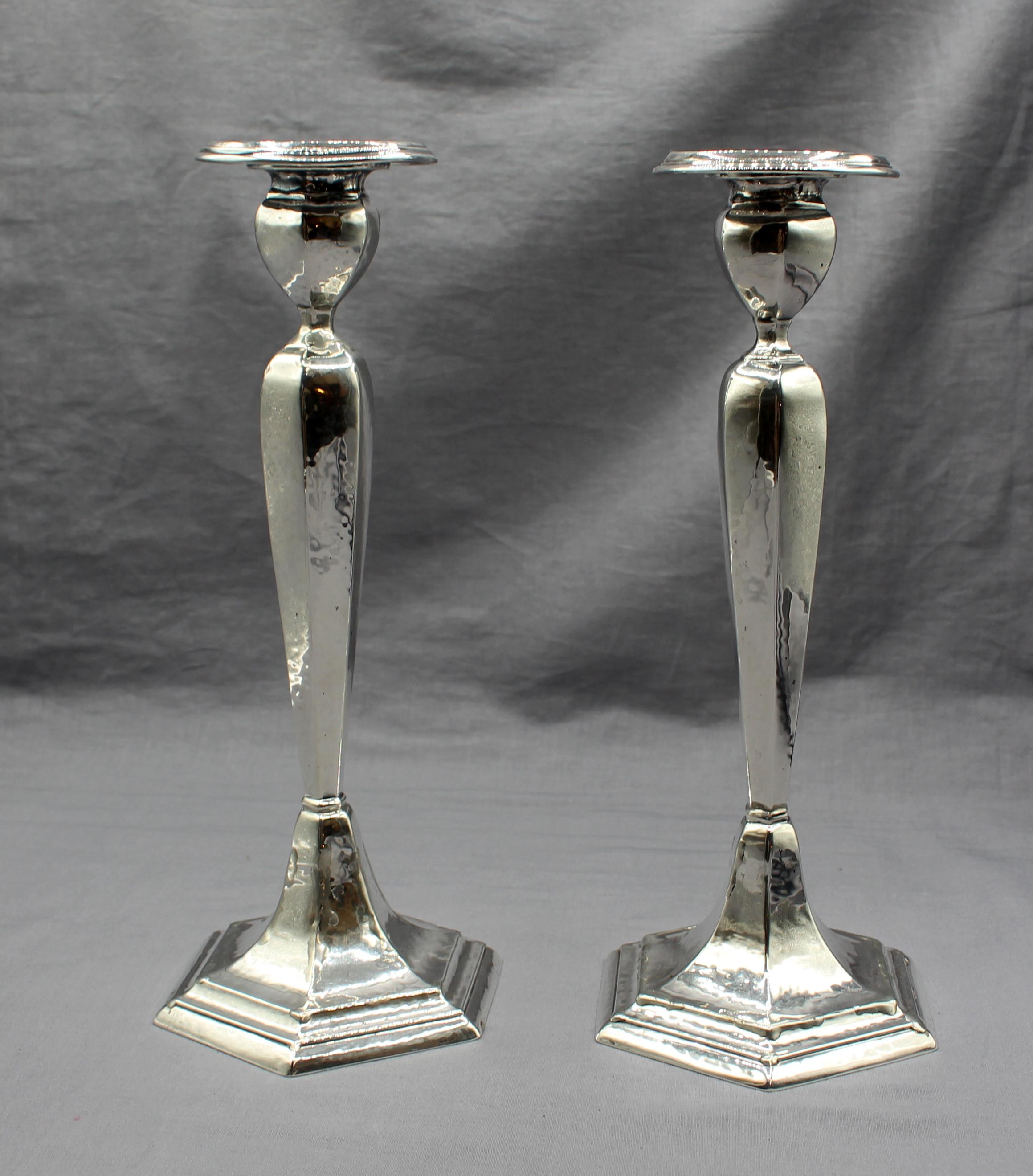 A pair of sterling silver weighted candlesticks by International, circa 1920s. Marked: Hand Hammered, Pitch Loaded Wood Reinforced. Hexagonal bases rise to circular bobeche. One with extensive professional repairs. Bobeche slightly wrinkly which may