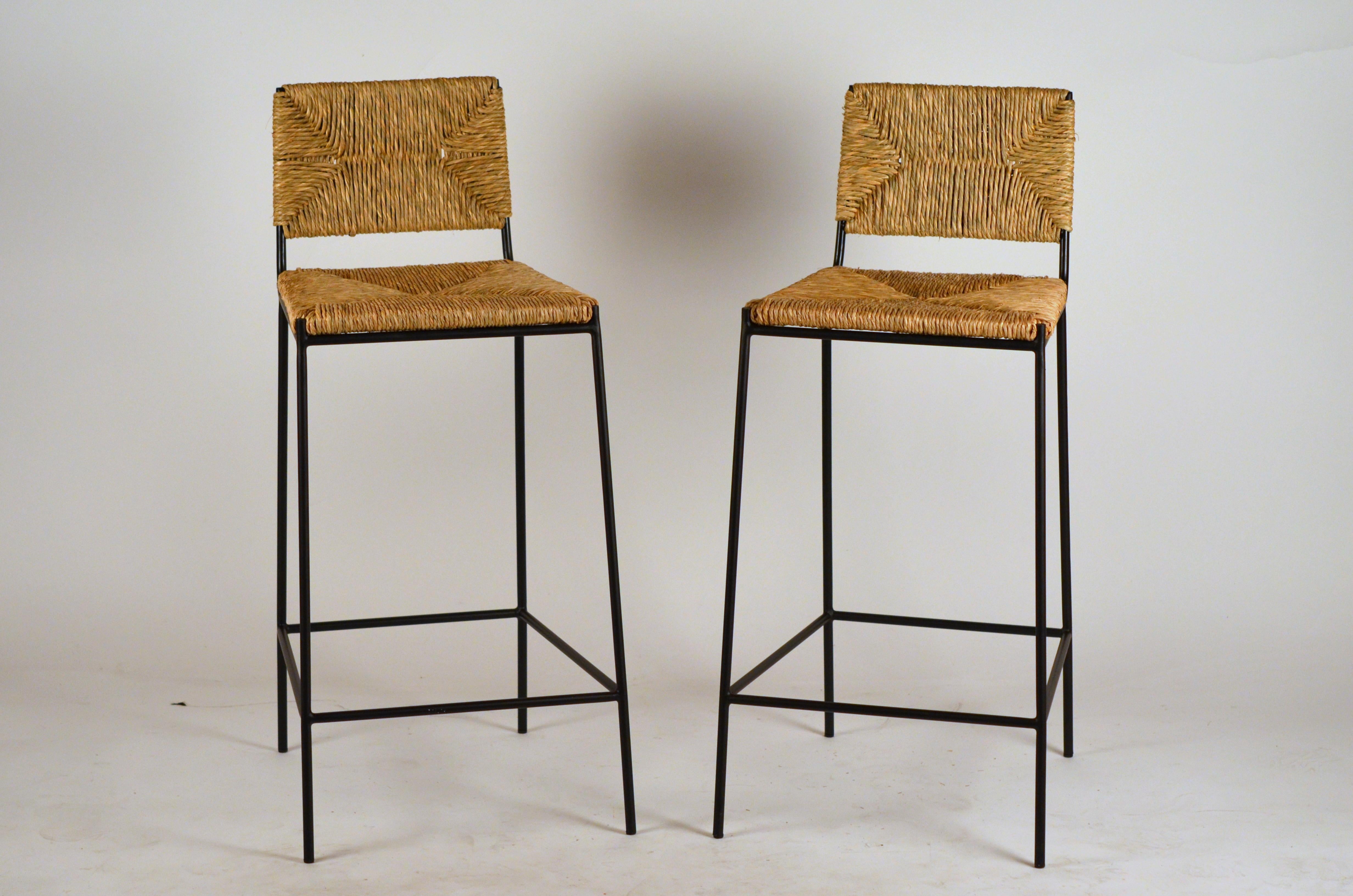Pair of 'Campagne' counter height stools by Design Frères.

Chic combination of slender but sturdy powder coated steel frames with handwoven rush seats and backs. Extra support under the rush seat for durability. Durable plastic caps on the feet