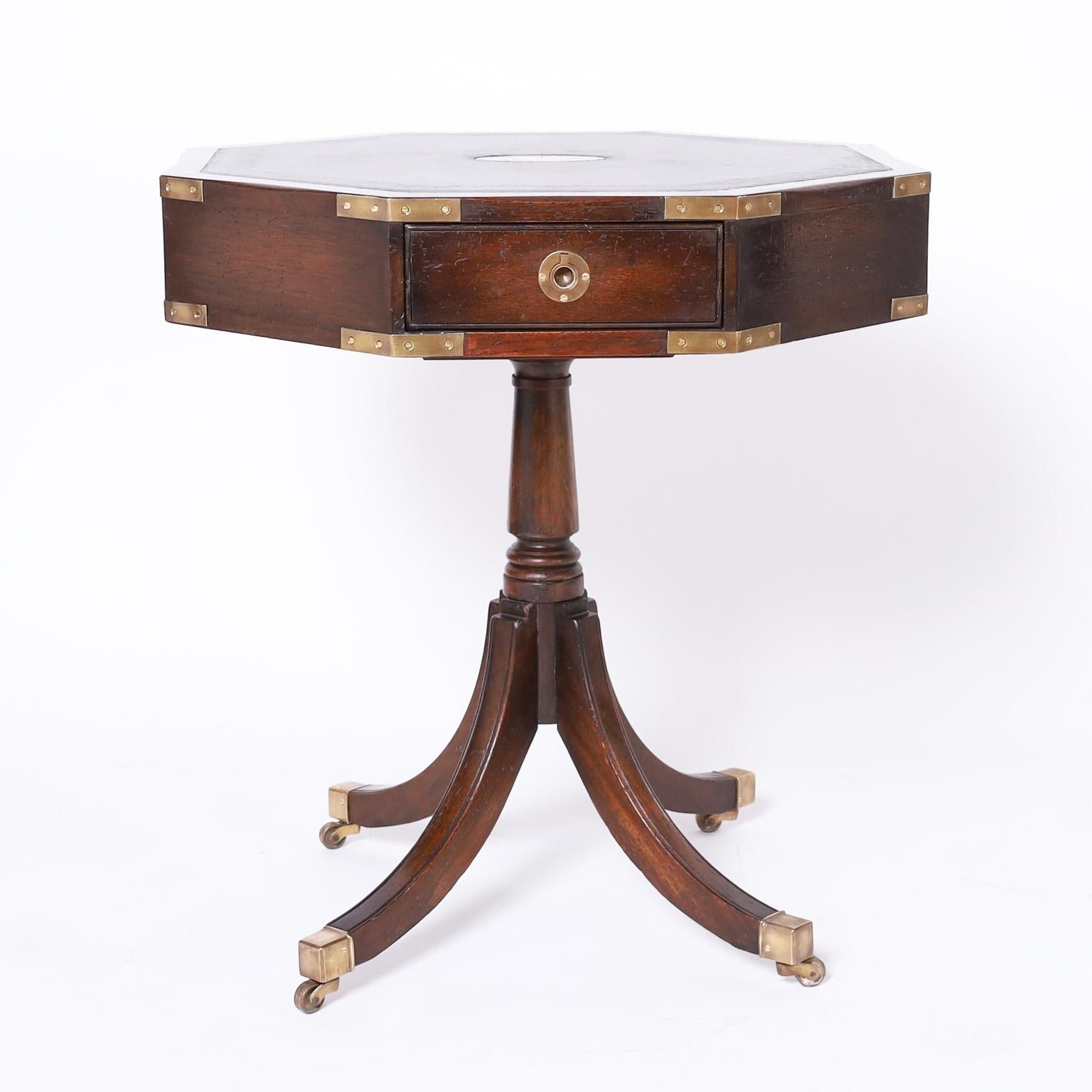 Impressive pair of English tables crafted in mahogany with dark green leather tops having oval brass medallions on an octagon case with four drawers having brass campaign hardware. The bases have turned pedestals and elegant Regency Sheraton style