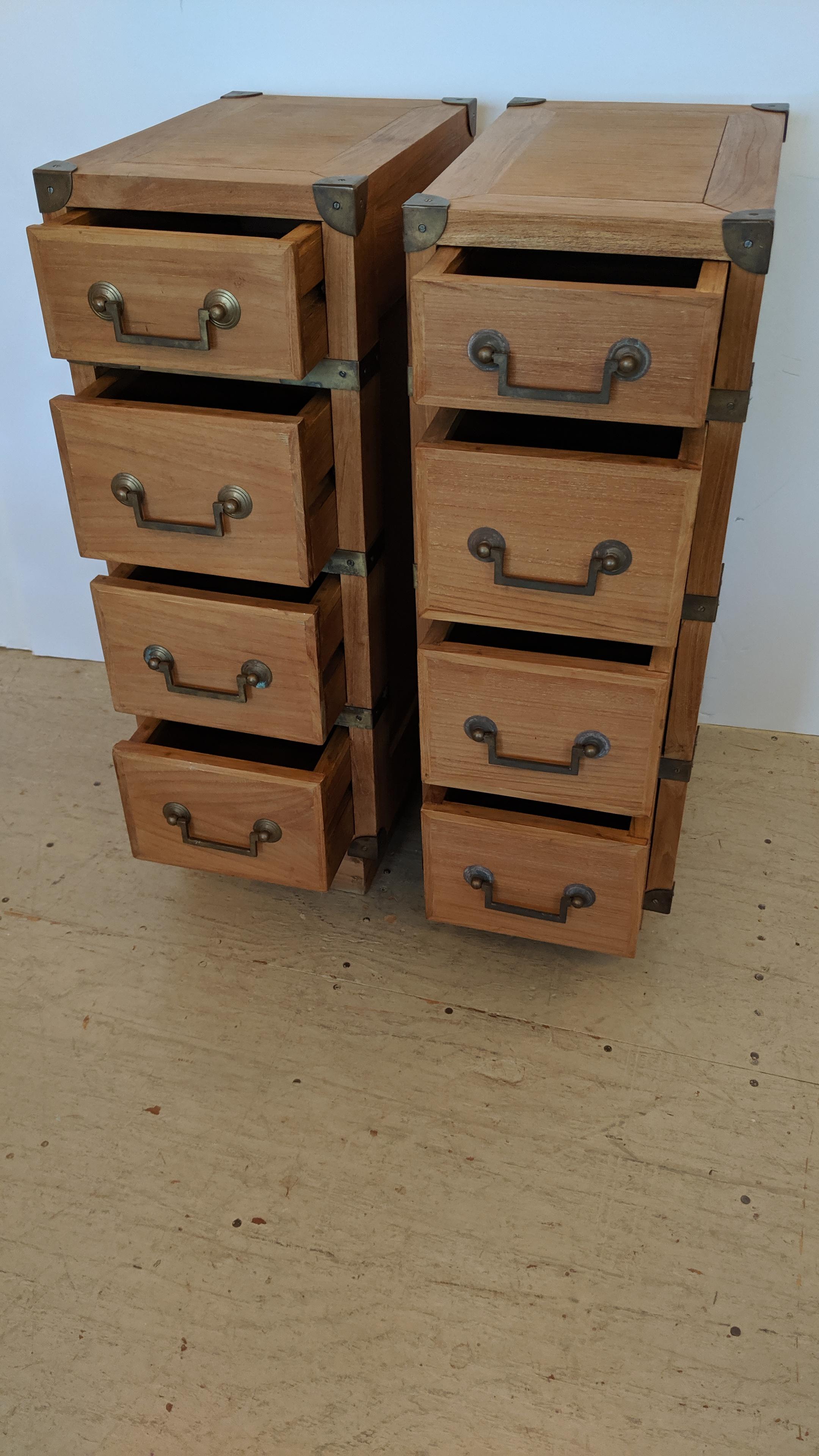 A pair of handsome versatile 4-drawer Campaign style tall and narrow chests, nightstands or end tables having brass hardware and light colored teak wood.