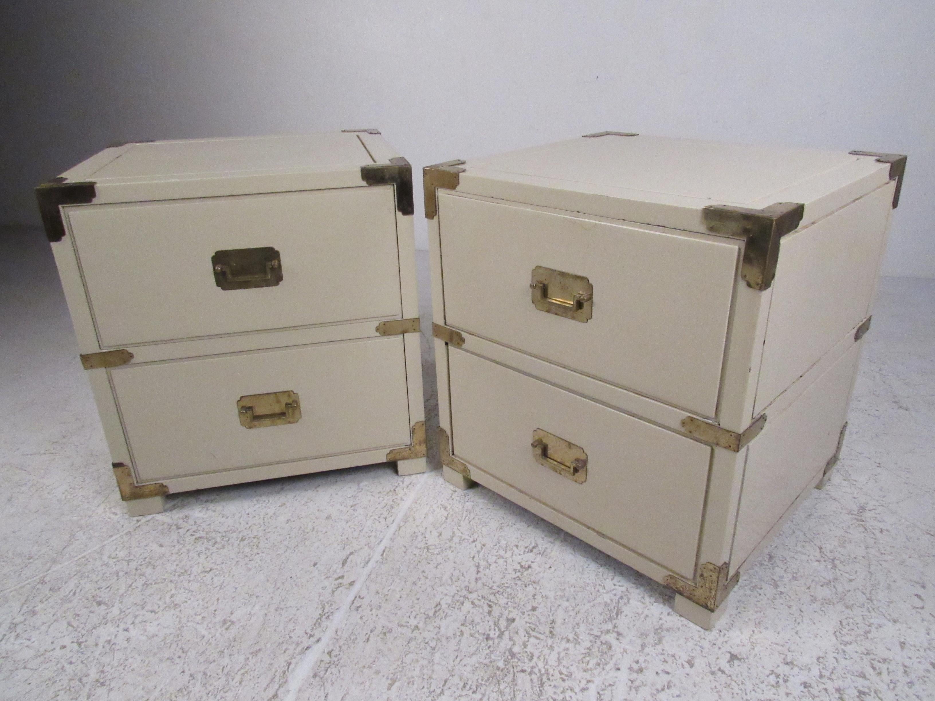 Attractive pair of crème color two-drawer Campaign style cabinets with brass hardware and finished backs. Perfect for use in a nightstand or end table application. Please confirm item location (NY or NJ) with dealer.