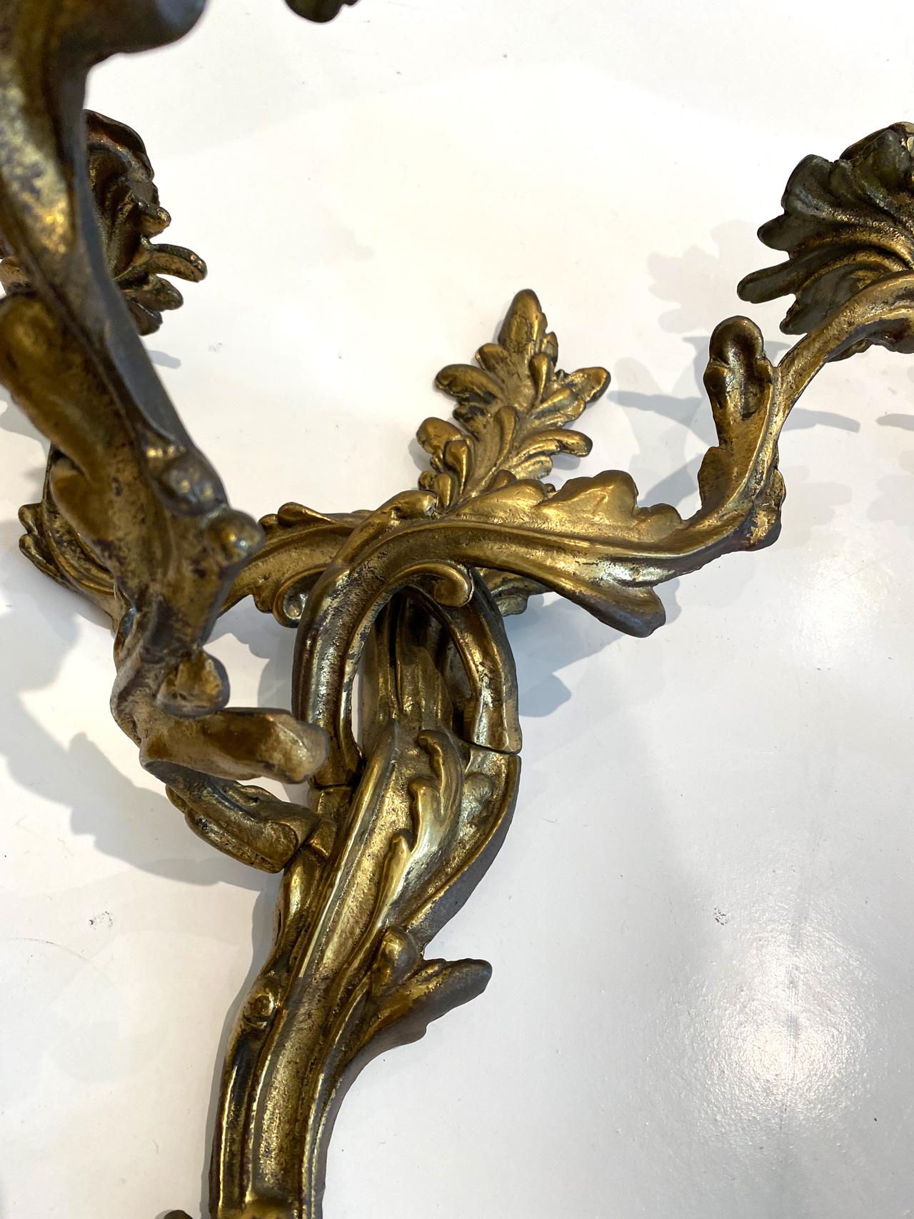 This is a beautiful pair of gilded bronze three arm articulating sconces. Can be electrified, but are perfect for real candles. Profiled and heavily ornamented wall brackets with three curved candlestick arms with leaf detail and large eaves bowls