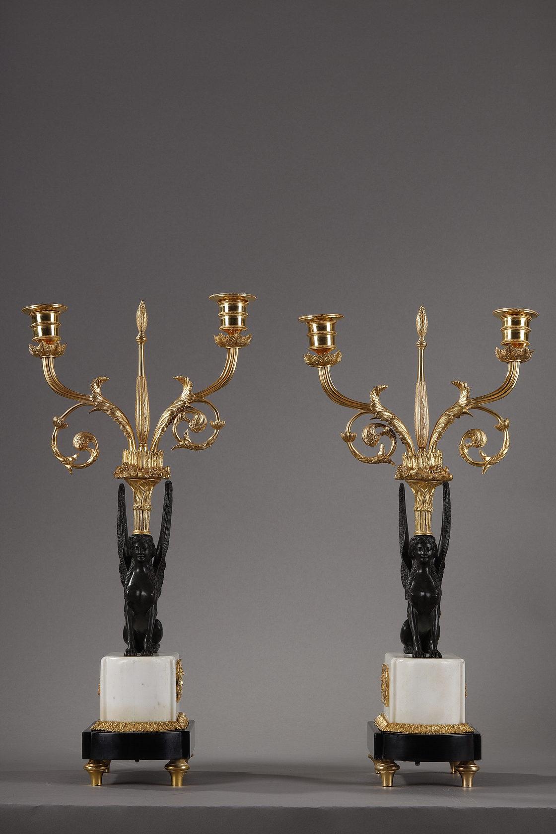 A pair of Directoire period gilt and patinated bronze and black and white marble candelabras. They present a decoration of winged sphinxes in patinated bronze carrying on their heads a motif of woven basket filled with fruits and feathers from which