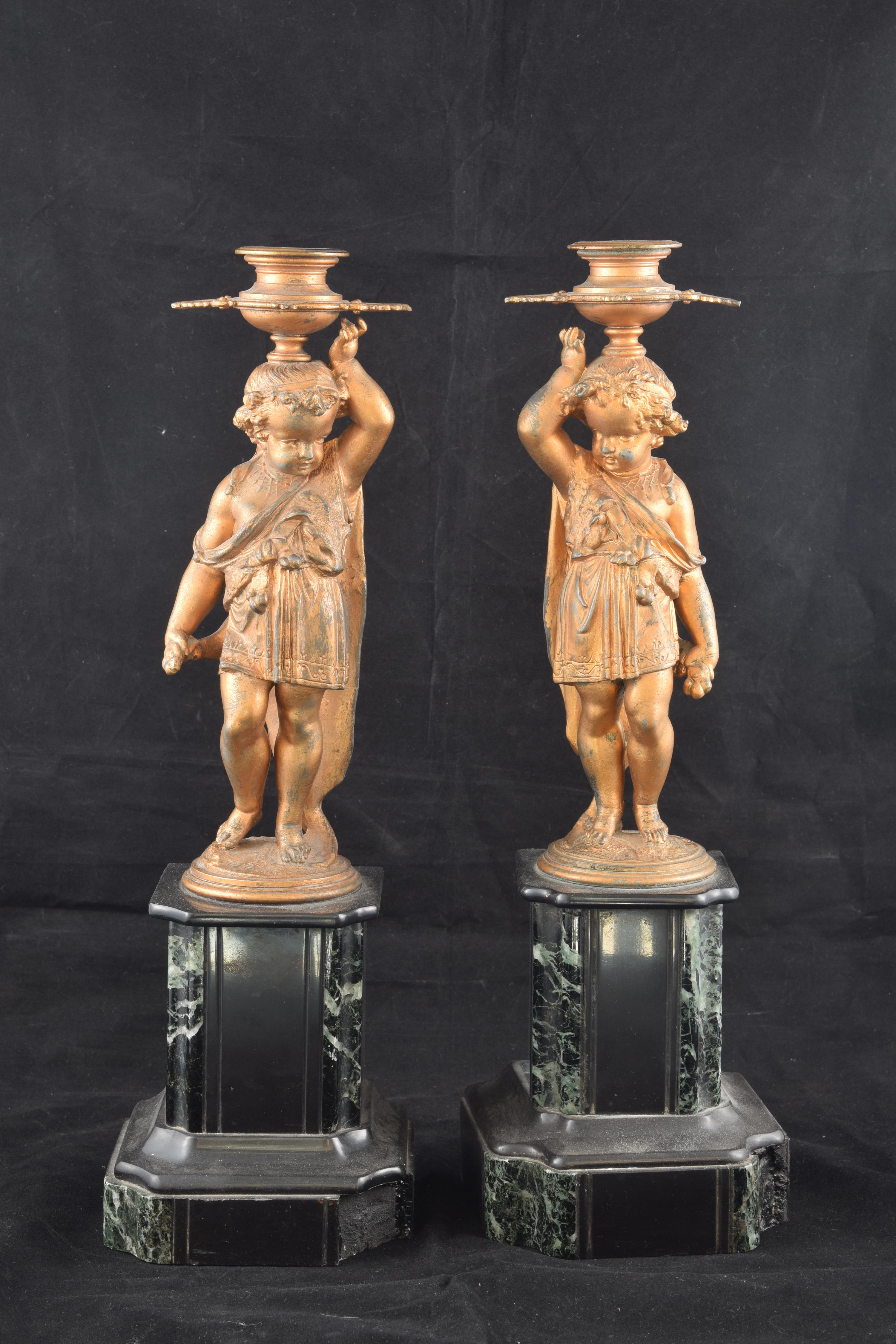 Pair of candlesticks made in calamine on dark marble bases that have two sculptures of children in similar positions. The proportions, positions, decorative elements, etc. of these two figures show a clear influence of models of French