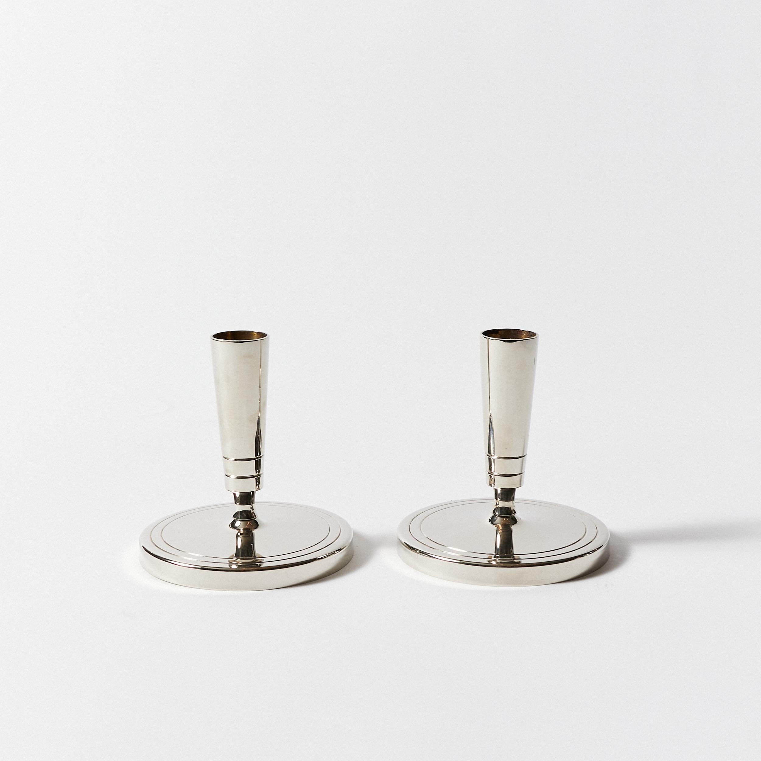 Set of two polished nickel candlesticks with a circular base and sinuous stem designed by Tommi Parzinger for Dorlyn Silversmiths.