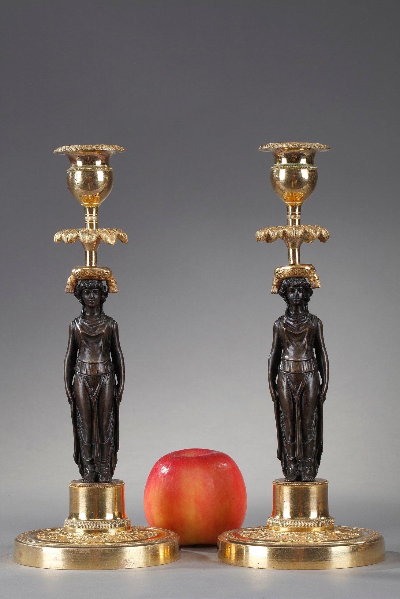 Pair of Charles X period torches in patinated and gilt bronze. The base is decorated with a border of palmettes and lotus. The shaft is decorated with caryatids representing vestals dressed in ancient tunics with their hair tied in a turban. In the