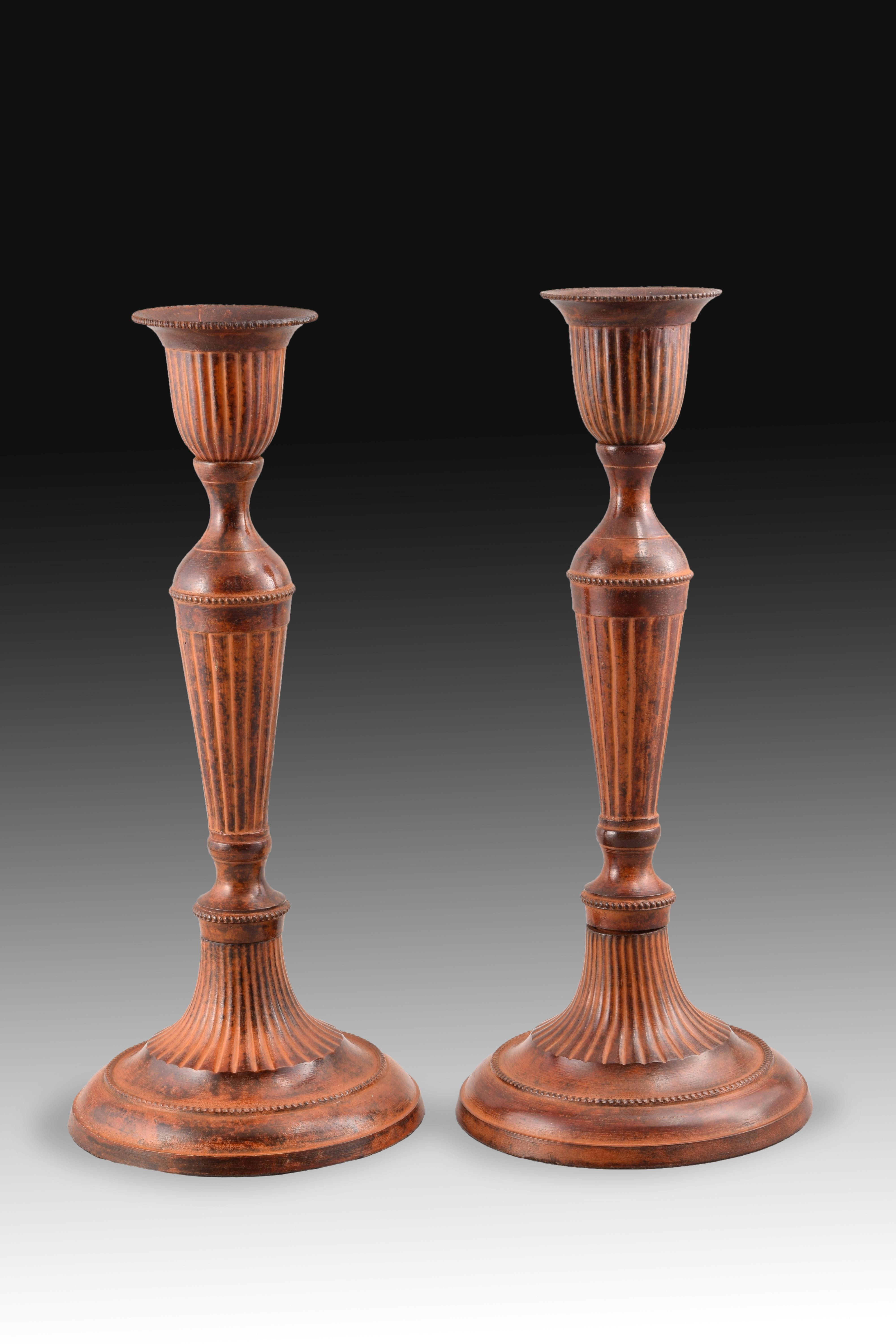 Pair of candlestick in patinated bronze.
The circular base shows a decoration based onmoldings and grooves, the latter element that is repeated by the barrel, which has been shaped into a circular stipe, and the vase that serves as the base for the