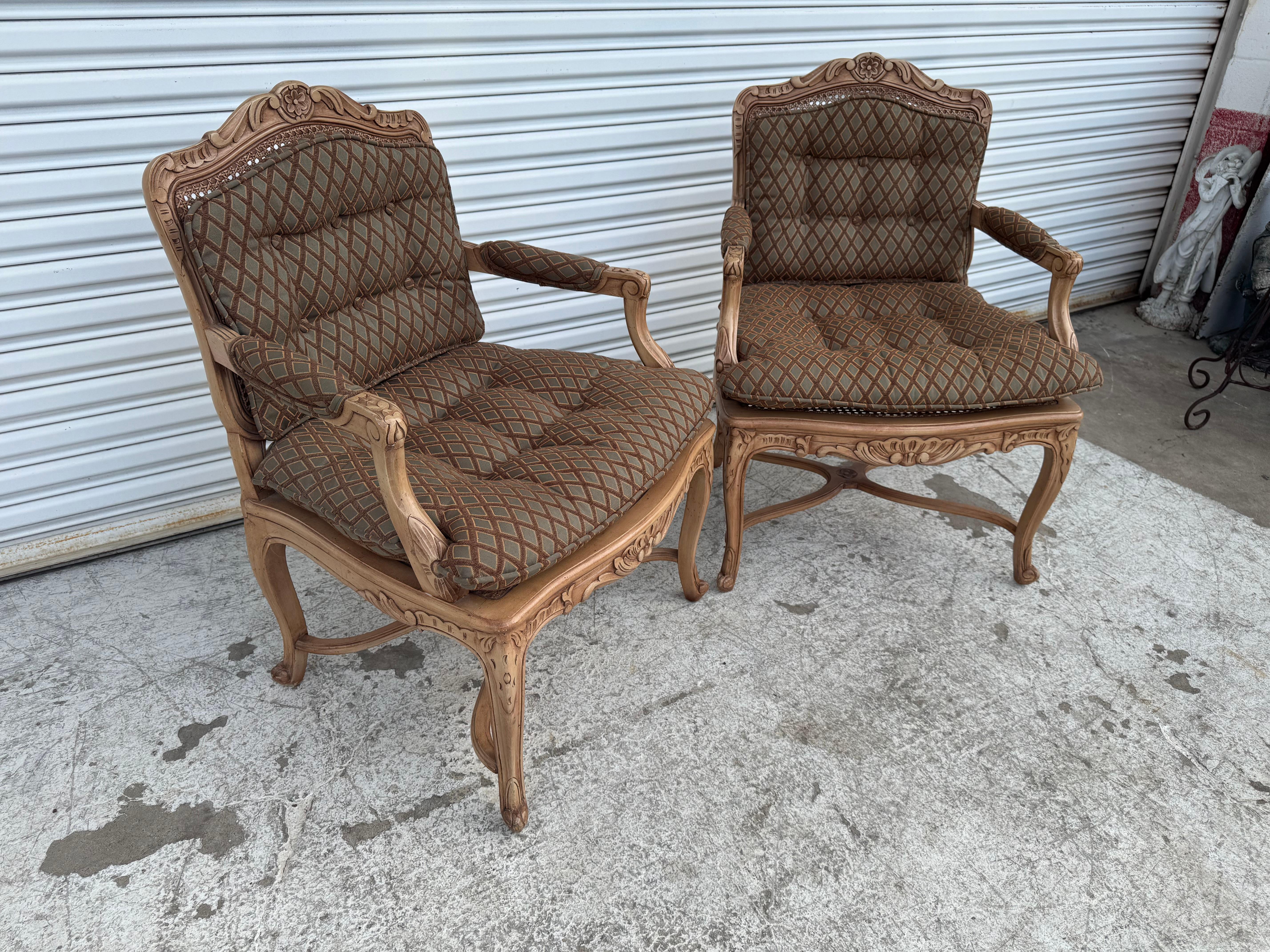Questa elegante coppia di poltrone con schienale in canna è caratterizzata da intricate cornici in legno intagliate con dettagli floreali e a volute, in un classico stile provinciale francese o Louis Cane XV. Le sedie sono dotate di cuscini morbidi
