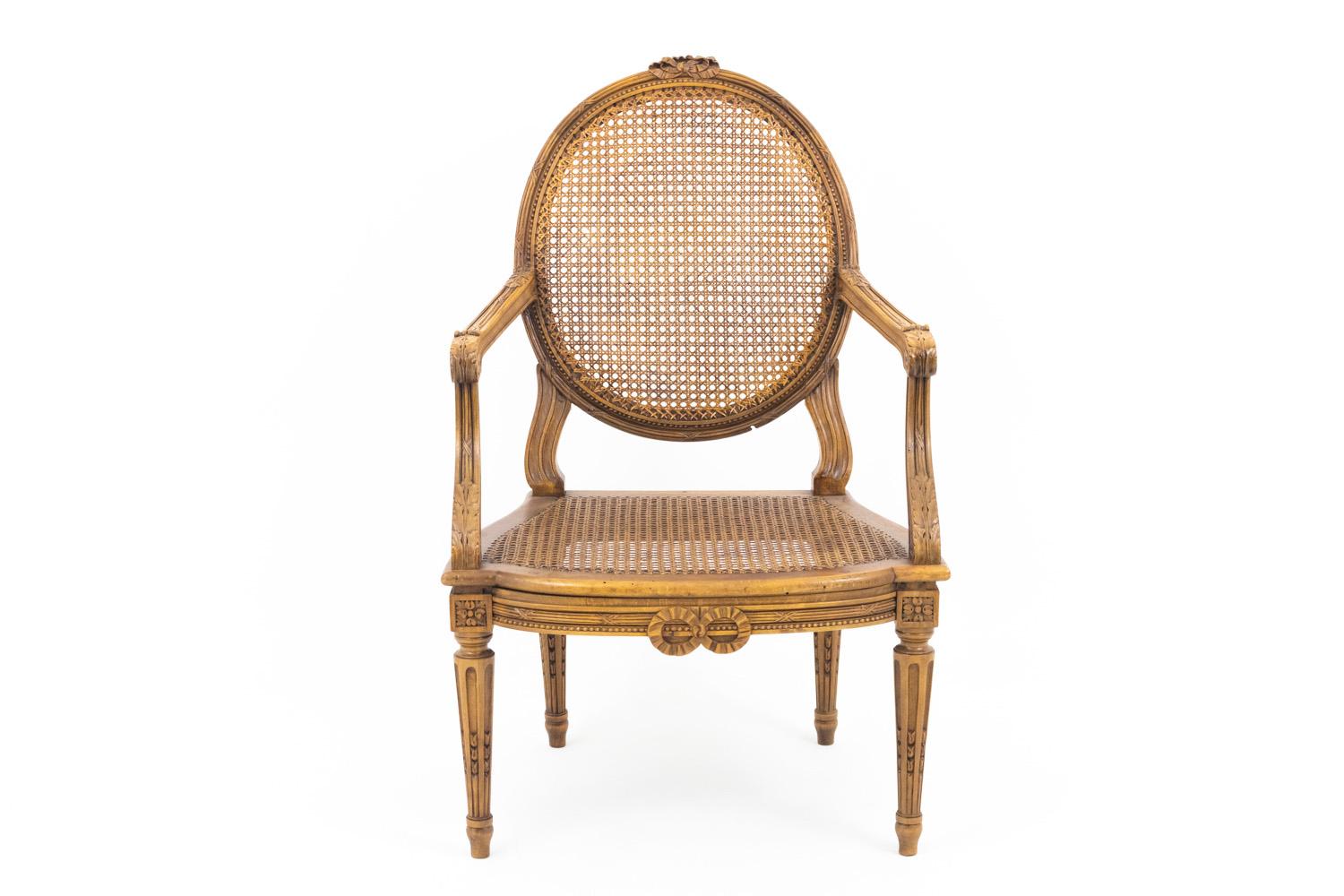 Pair of cane Louis XVI style walnut armchairs standing on four fluted tapered legs carved with chandelles (candles motifs) topped by joints carved of rosettes. Medallion back. Seat rail and stiles adorned with ribboned bulrushes, beads frieze and