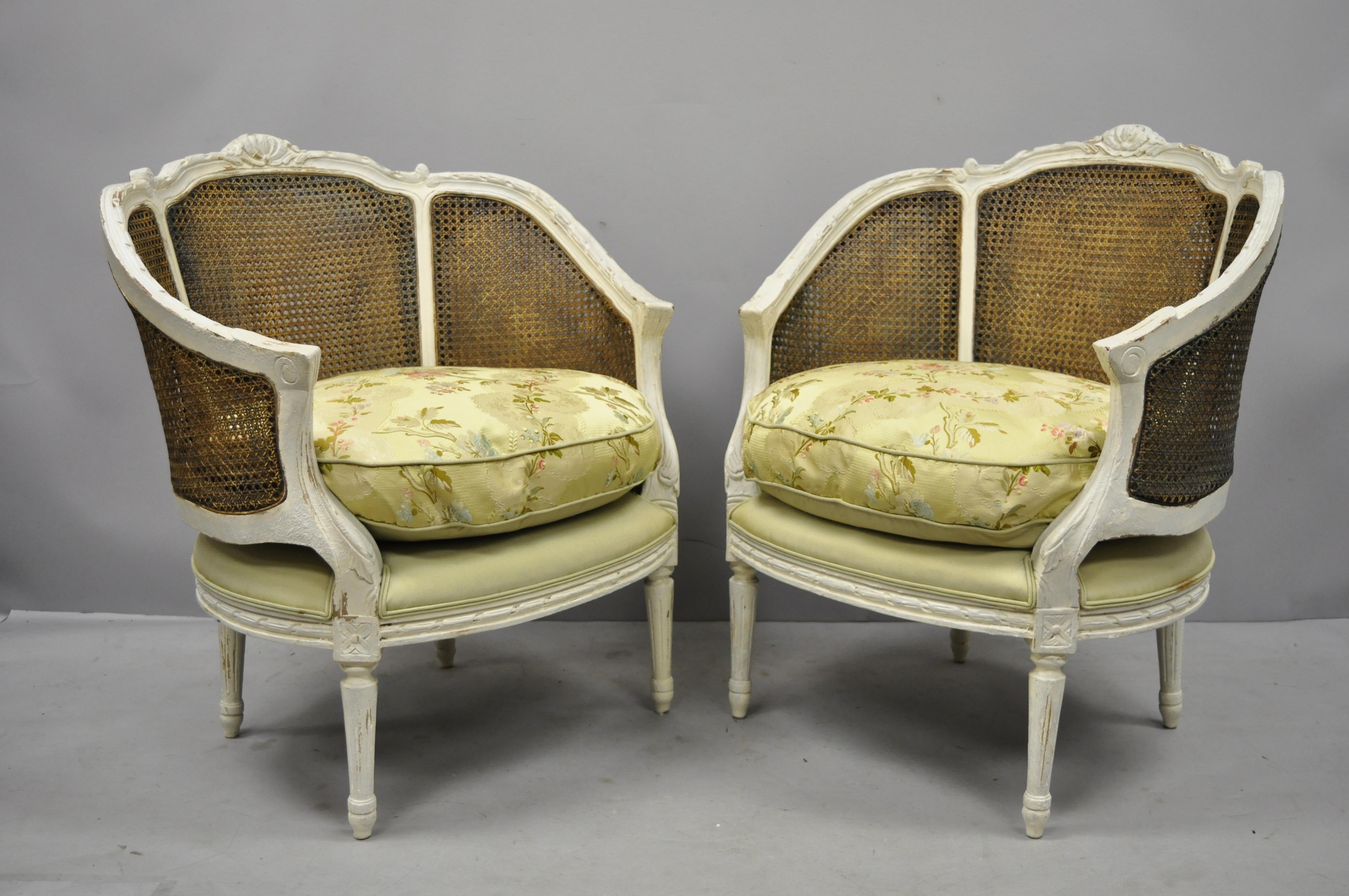 Pair of caned French Louis XVI style white distress painted Bergere salon chairs. Items feature cane backs, white painted distressed finish, loose cushions, solid wood construction, tapered legs, great style and form, circa Mid-20th century.