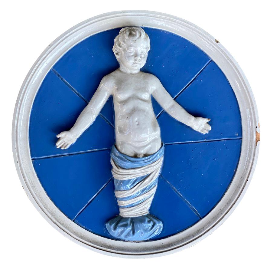 Signed on reverse. Blue ground and featuring children. Copies of Andrea della Robbia work for the loggia of the Ospidale degli Innocenti in Florence.