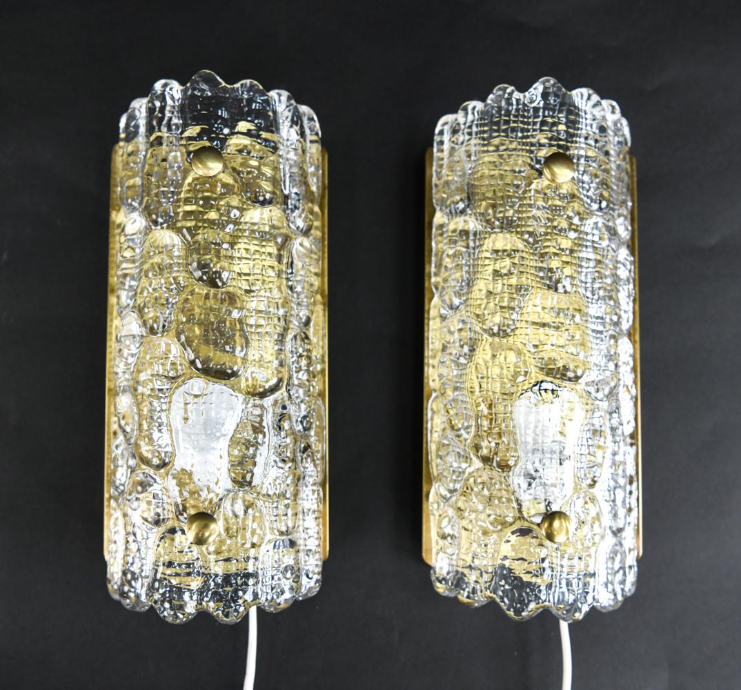 A pair of sconces designed by Carl Fagerlund for Orrefors. A classic Swedish design of arched bodies with scalloped top and bottom edges, in heavily textured clear ice glass mounted on brass.
