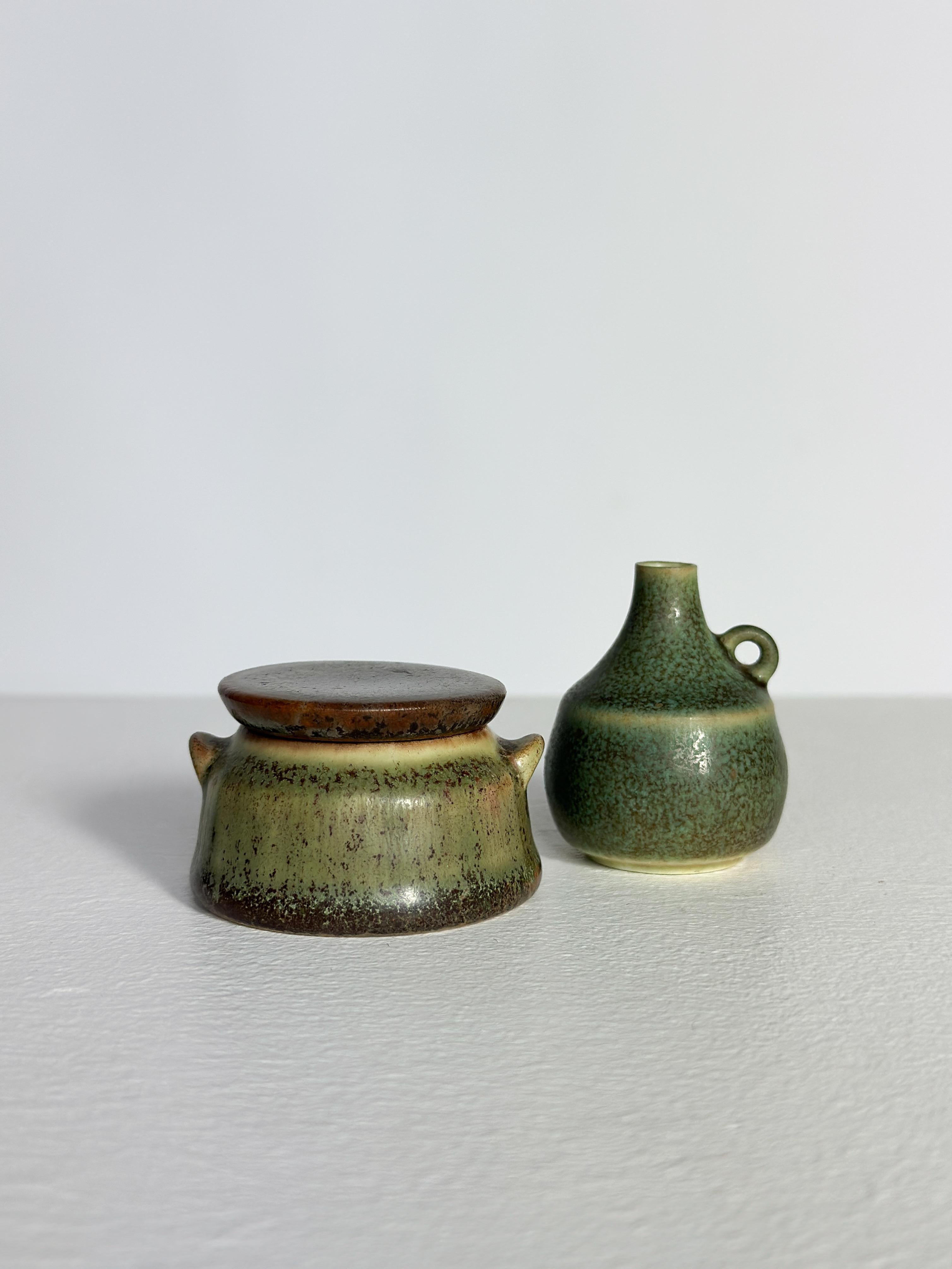 Una coppia di ceramiche in miniatura di Carl-Harry Stålhane per Rörstrand Sweden alla fine degli anni '50.

Vaso in gres con coperchio: H. 3,2 cm, P. 5,3 cm
Vaso in gres con manico: H. H. 4.7 cm, P. 3.7 cm

L'ultima foto mostra il nostro attuale