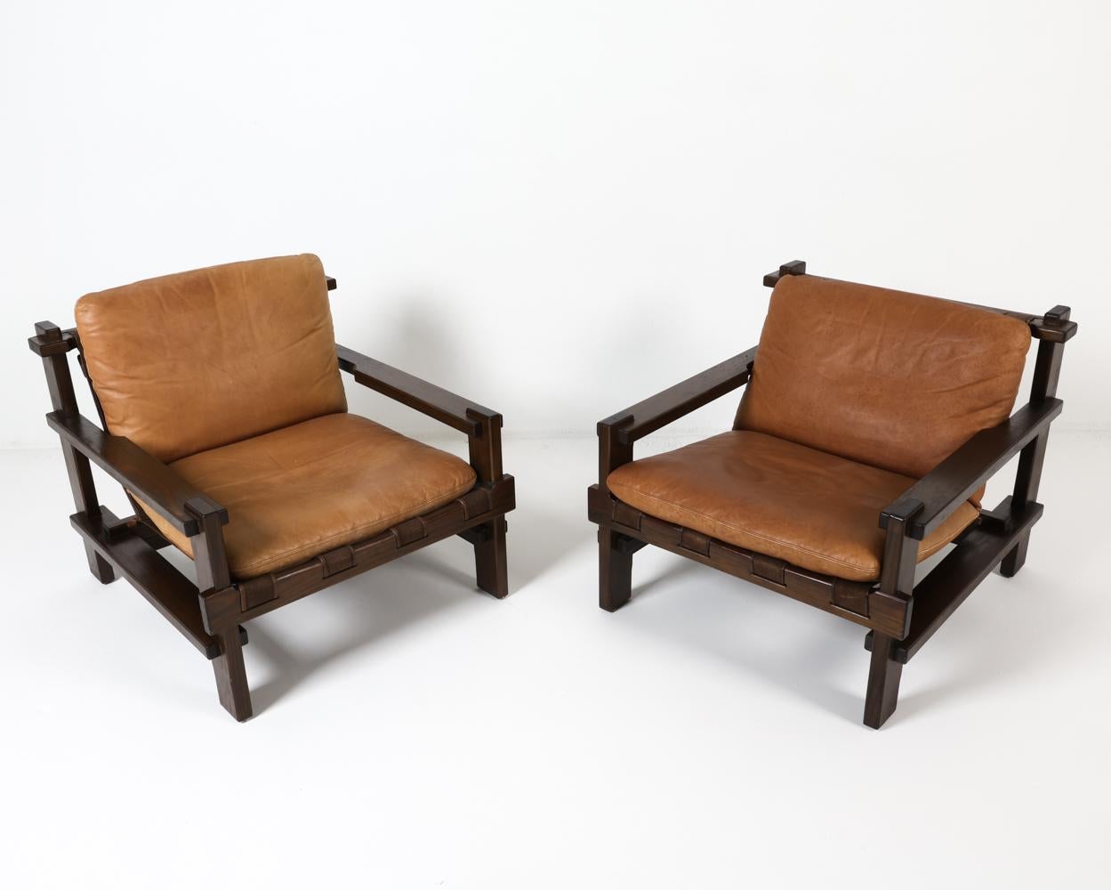 This striking pair of lounge chairs, designed by the esteemed Carl Straub, exemplify the refined Danish design aesthetic of the 1970s. These chairs, with their distinctive combination of dark-stained pine frames, supple tan leather cushions, and