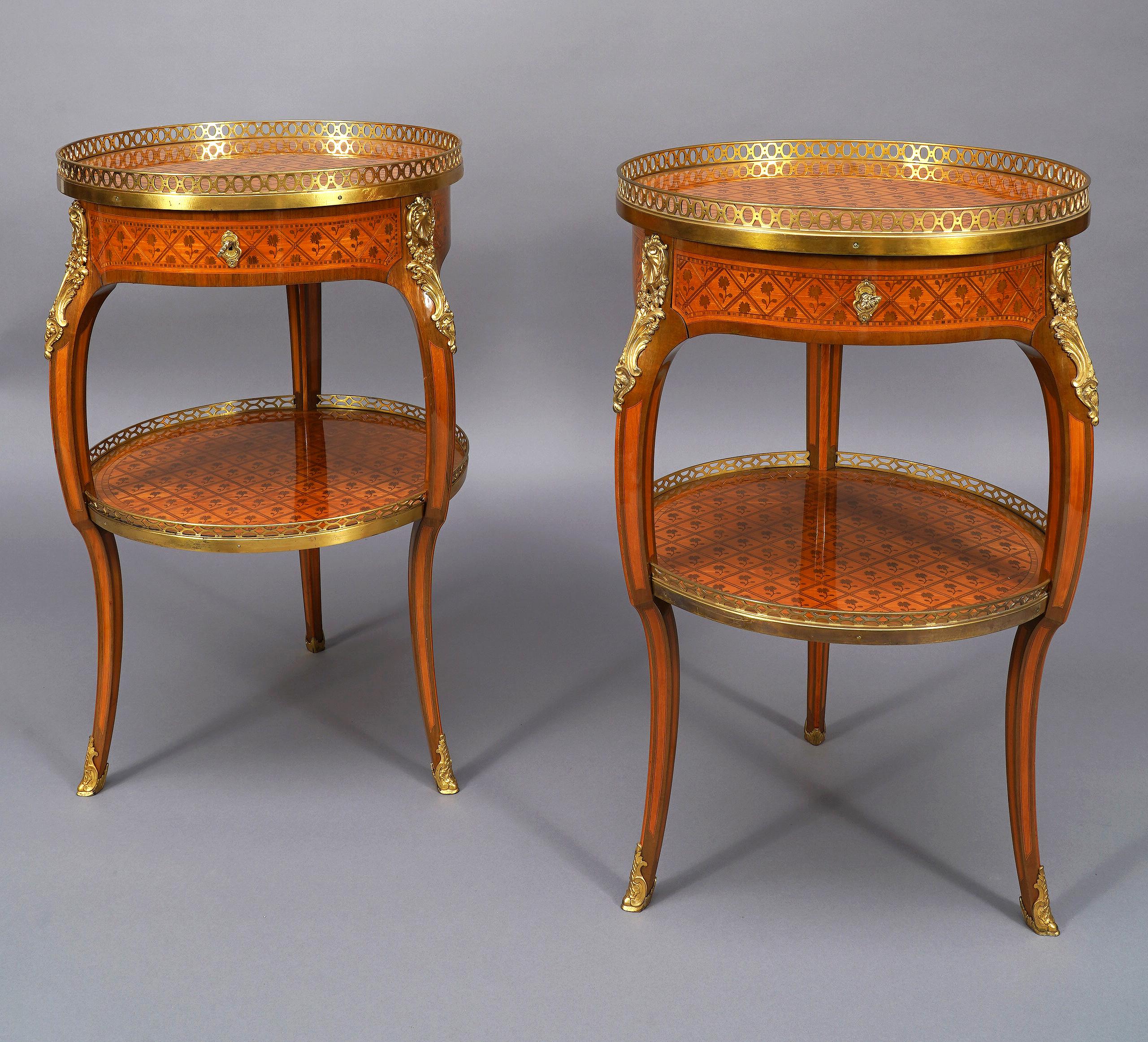 Elegante paire de tables de style Louis XV en marqueterie, avec une belle ornementation de bronze ciselé et doré, ouvrant par un tiroir en ceinture. Le plateau, ainsi que l'entretoise, sont entourés d'une galerie ajourée en bronze doré et décorée