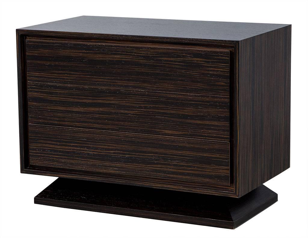 These modern nightstands are custom-made. Each has beveled edges on the case and base and is finished in Macassar in a rich satin finish. A simple yet refined piece, it is also functional with two soft-close walnut drawers. A perfect fit for any