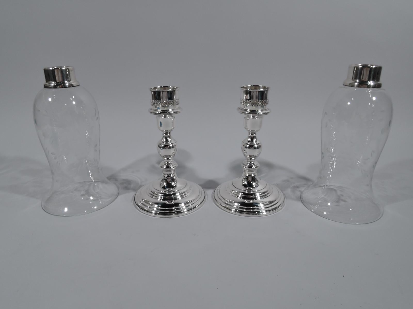 Pair of sterling silver candlesticks with glass shades, circa 1940. Retailed by Cartier in New York. Each: Baluster shaft on stepped and raised foot engraved with script monogram. Shades ovoid with flared rim; acid-etched stylized flowers. Perfect