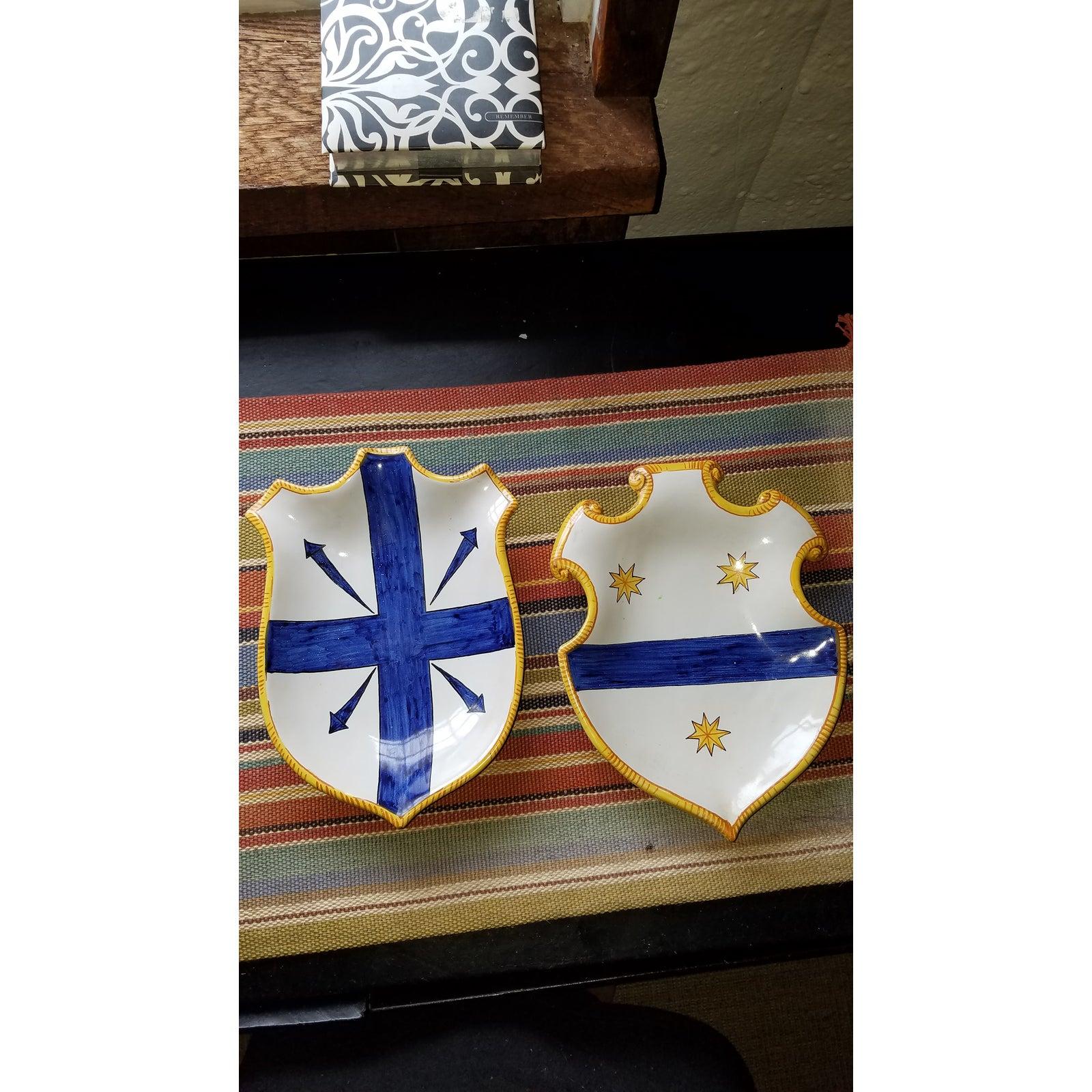 An unusual pair of Italian glazed and hand painted terracotta cartouche shield form wall plates in white, yellow and cobalt, signed on bottoms.