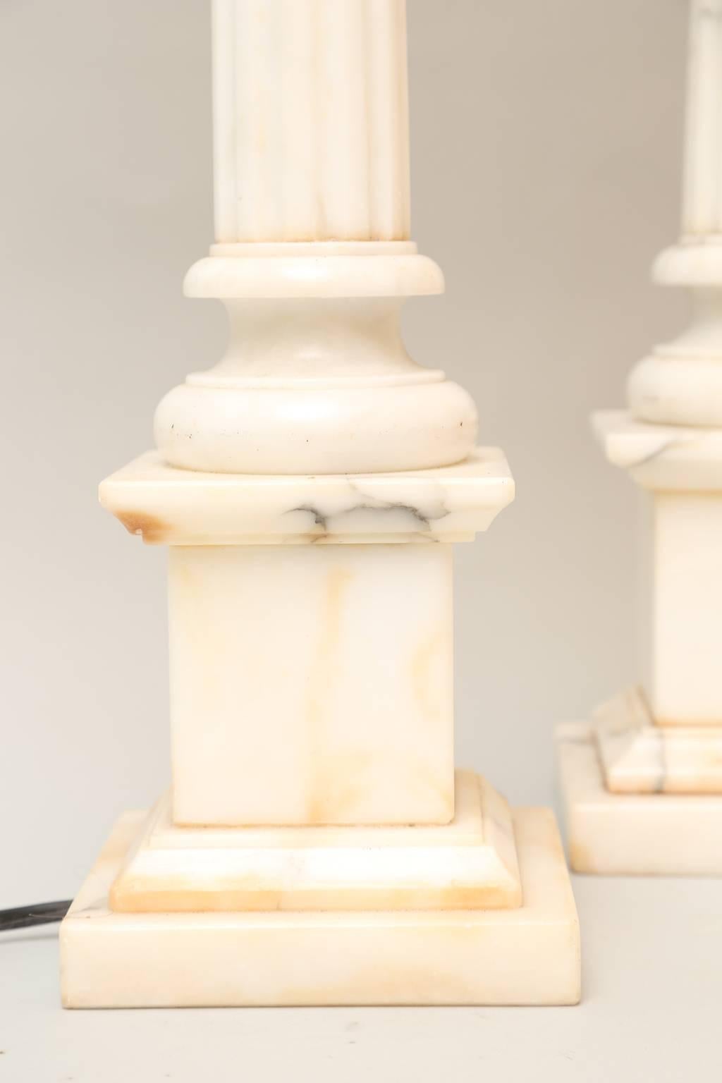 Pair of neoclassical style lamps, of carved alabaster, each a fluted column, with Ionic capital, ending in round foot, raised on square plinth base. 

Stock ID: D1233.