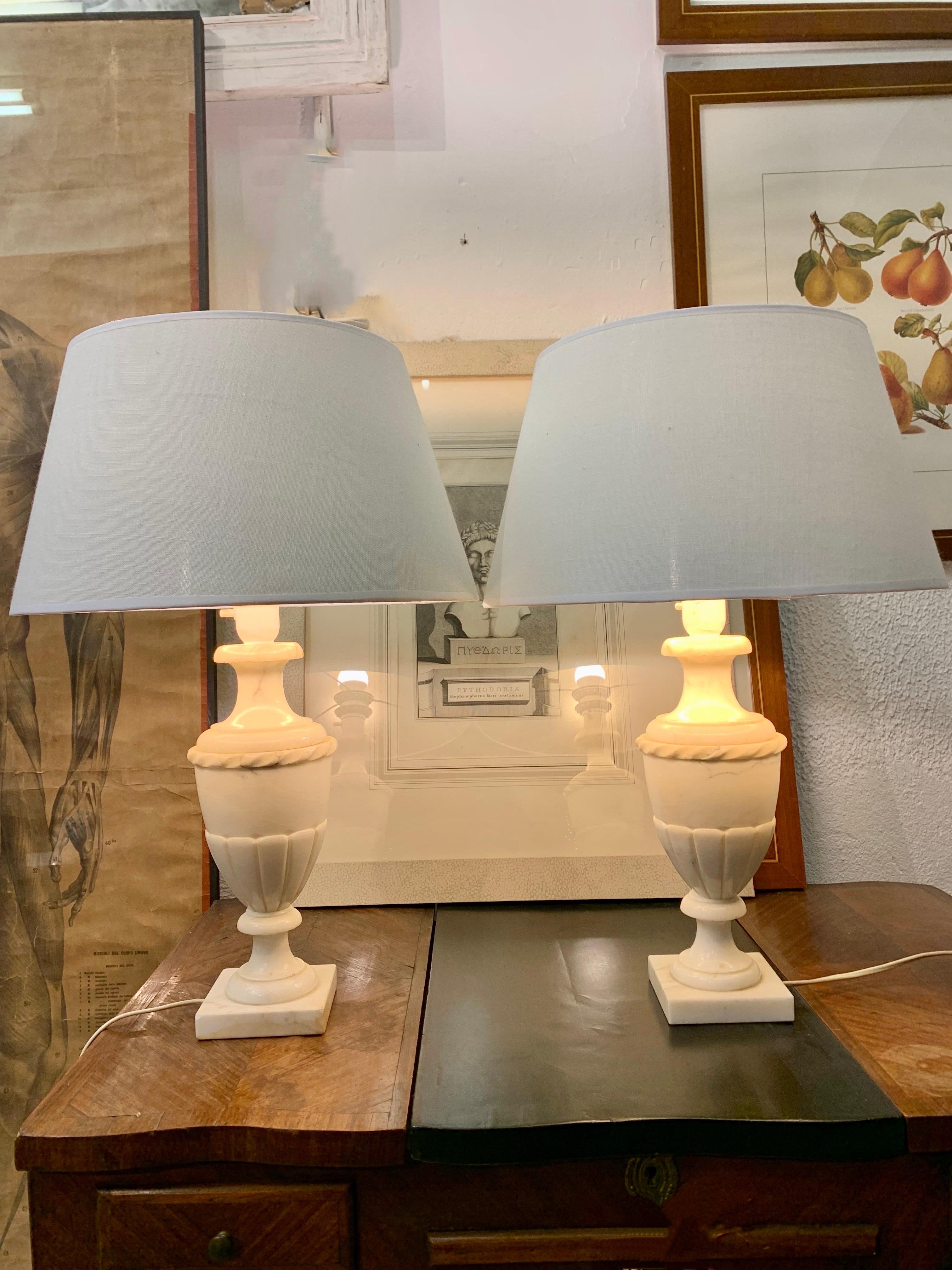 A pair of table lamps in carved alabaster, garland and gullonado decoration. 
The lamp shades in White plasticized linen and gold interior. 
The measurements are with the lampshade included, without the lampshade, the measurement is 36 cm high x 12