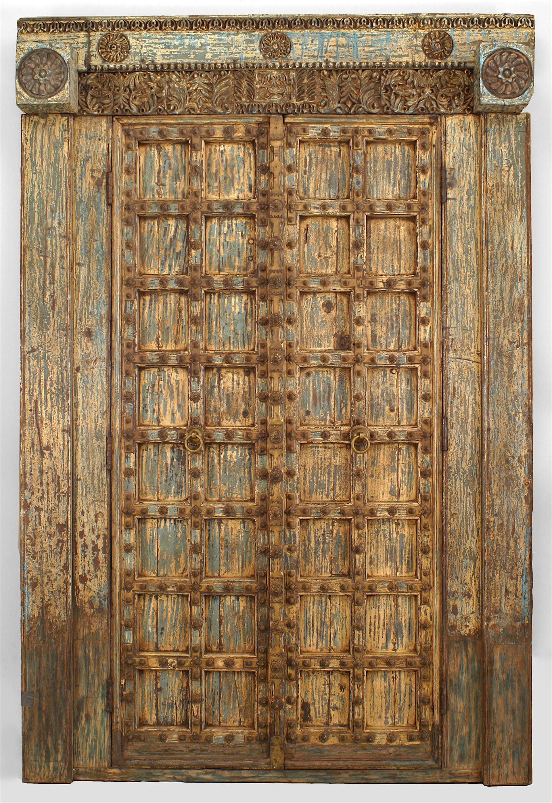 Paire de portes asiatiques (peut-être indiennes) (18/19ème siècle) peintes et sculptées en bleu et blanc dans un cadre avec un fronton séparé décoré de grandes têtes de clous et de garnitures en laiton (PRIX POUR LA PAIRE).
