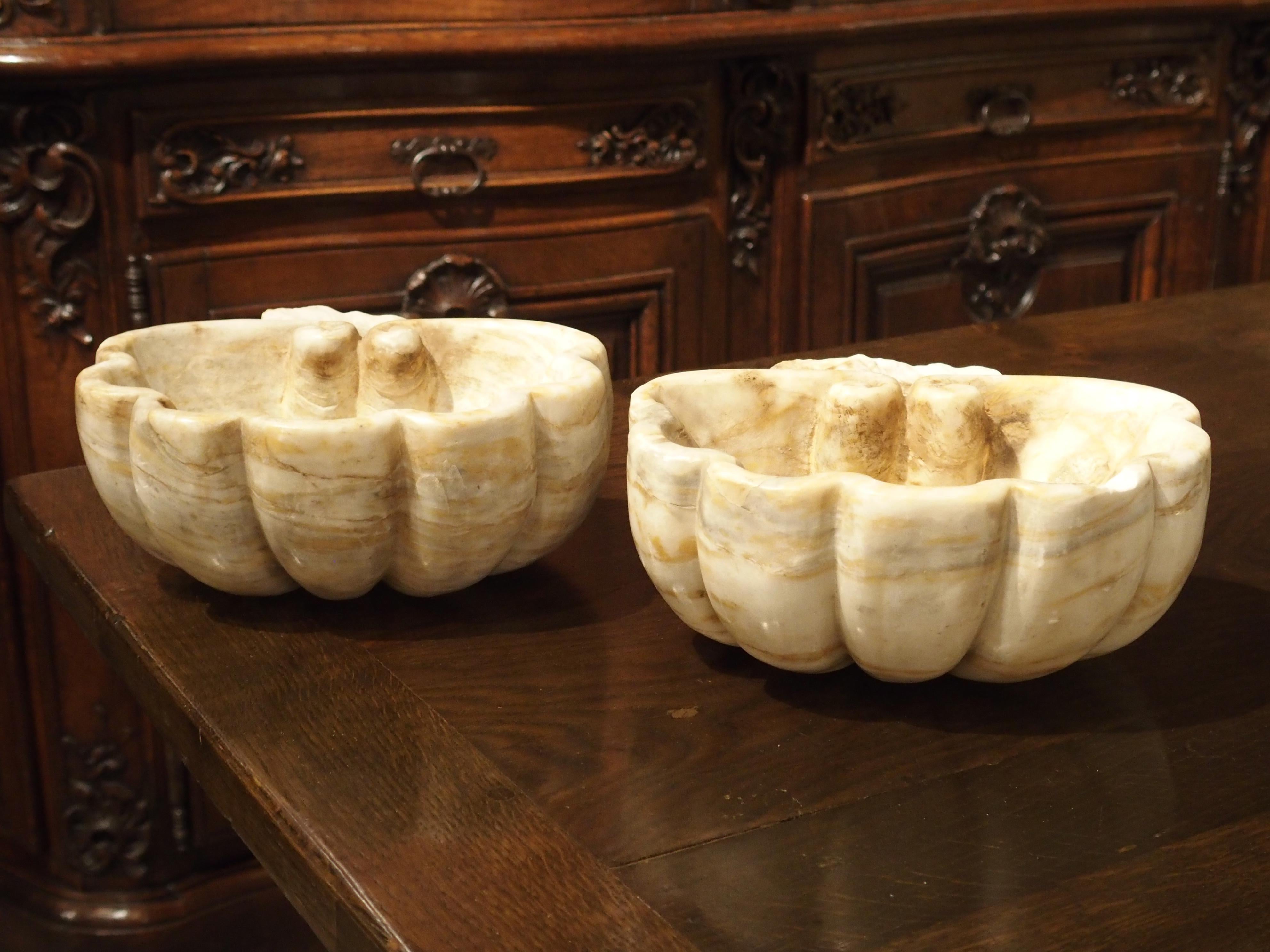 Small marble basins like these were probably originally used for holding holy water in Catholic Churches. They are in the shape of stylized shells with gadrooned lobes. You can see where the backs are rough cut, as if removed from the wall. Today
