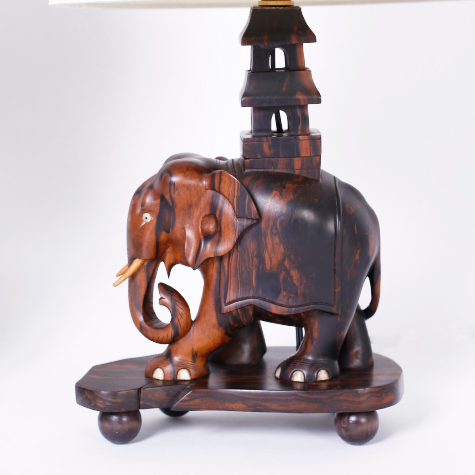 Exotic pair of antique table lamps carved in Coromandel wood with its distinctive dramatic grain depicting an elephant, with bone details, carrying a pagoda like structured walking on a biomorphic base with ball feet.