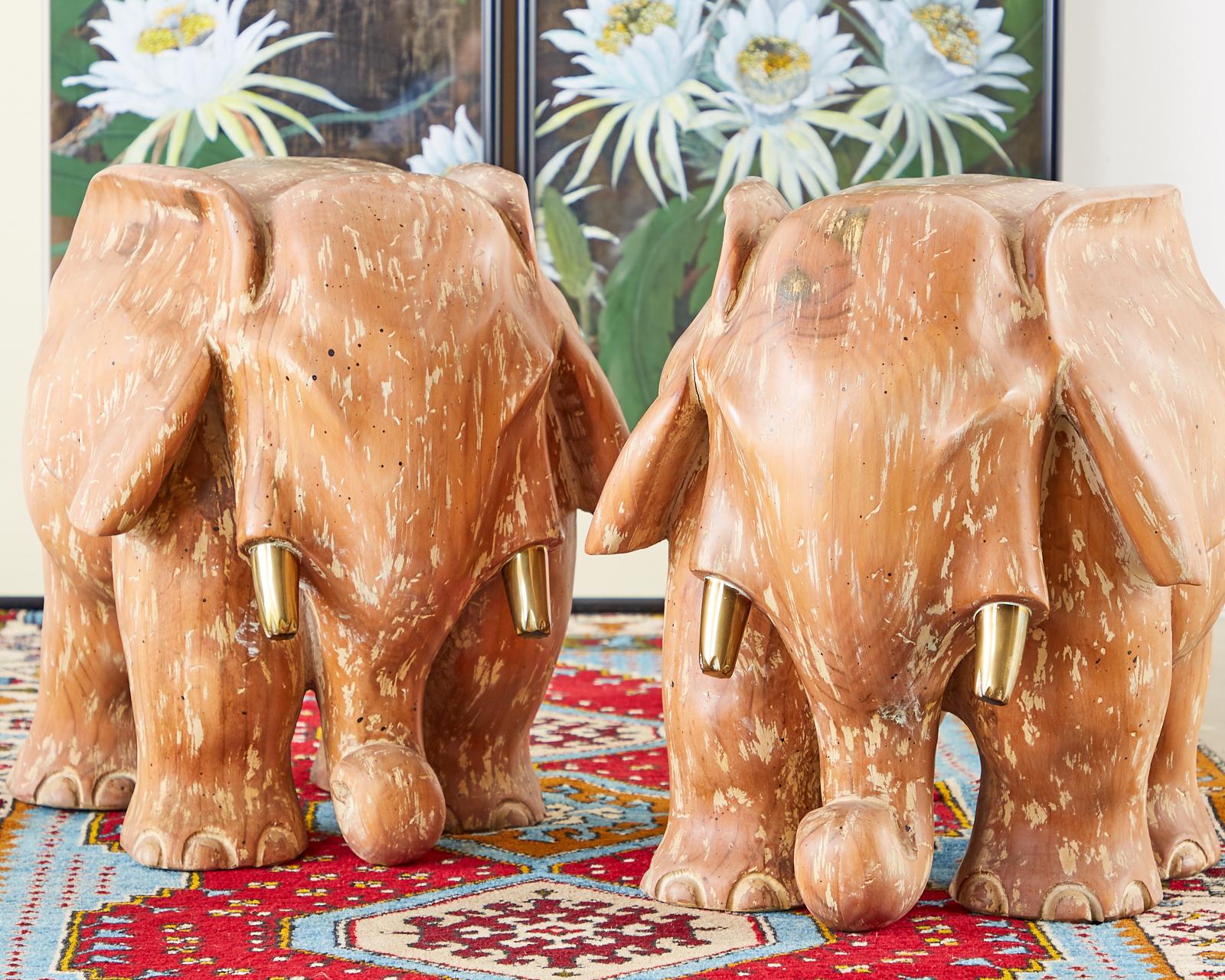 Whimsical pair of carved wooden elephant sculptures featuring a Cerused finish. Each elephant is depicted standing with large ears and brass tusks. Could be used separately with round panes of glass or together with one large pane as a cocktail