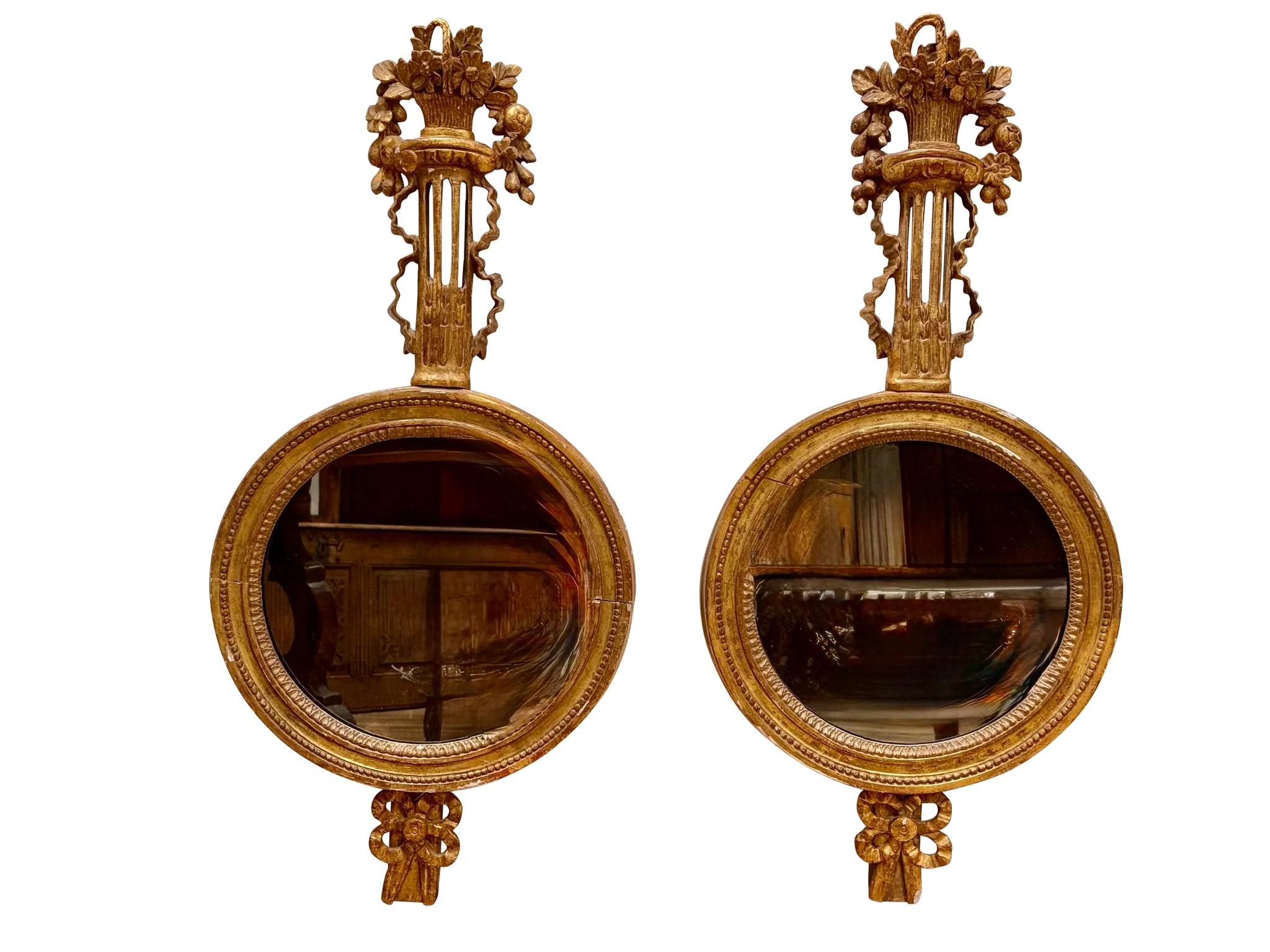 Paire de miroirs sculptés et dorés, probablement italiens, 19e siècle, chacun avec un panneau de verre circulaire sous une colonne cannelée poussant du feuillage à partir d'un vase.
