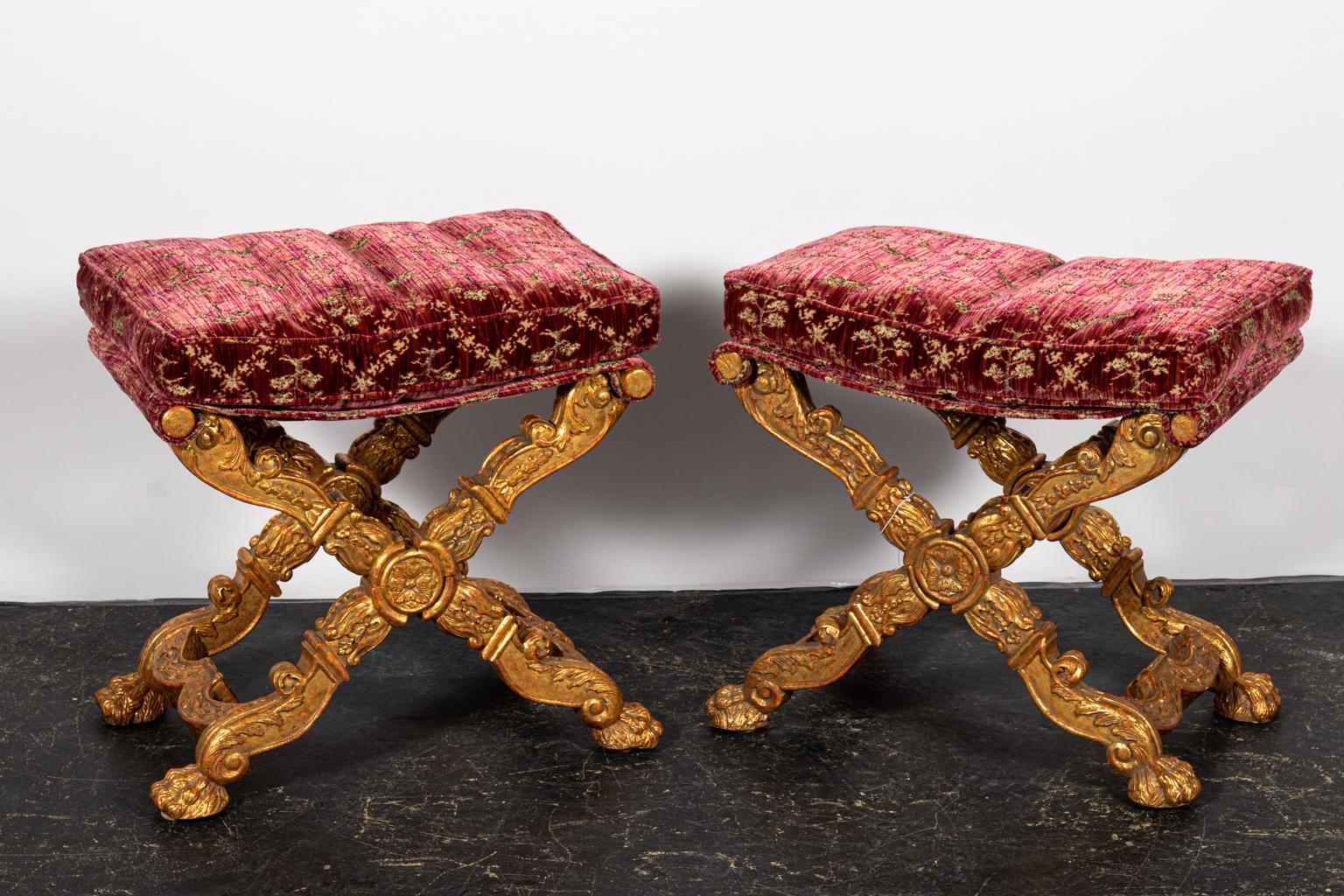 Pair of carved giltwood x-base stools upholstered in rose velvet. Please note of wear consistent with age including minor gilt loss.