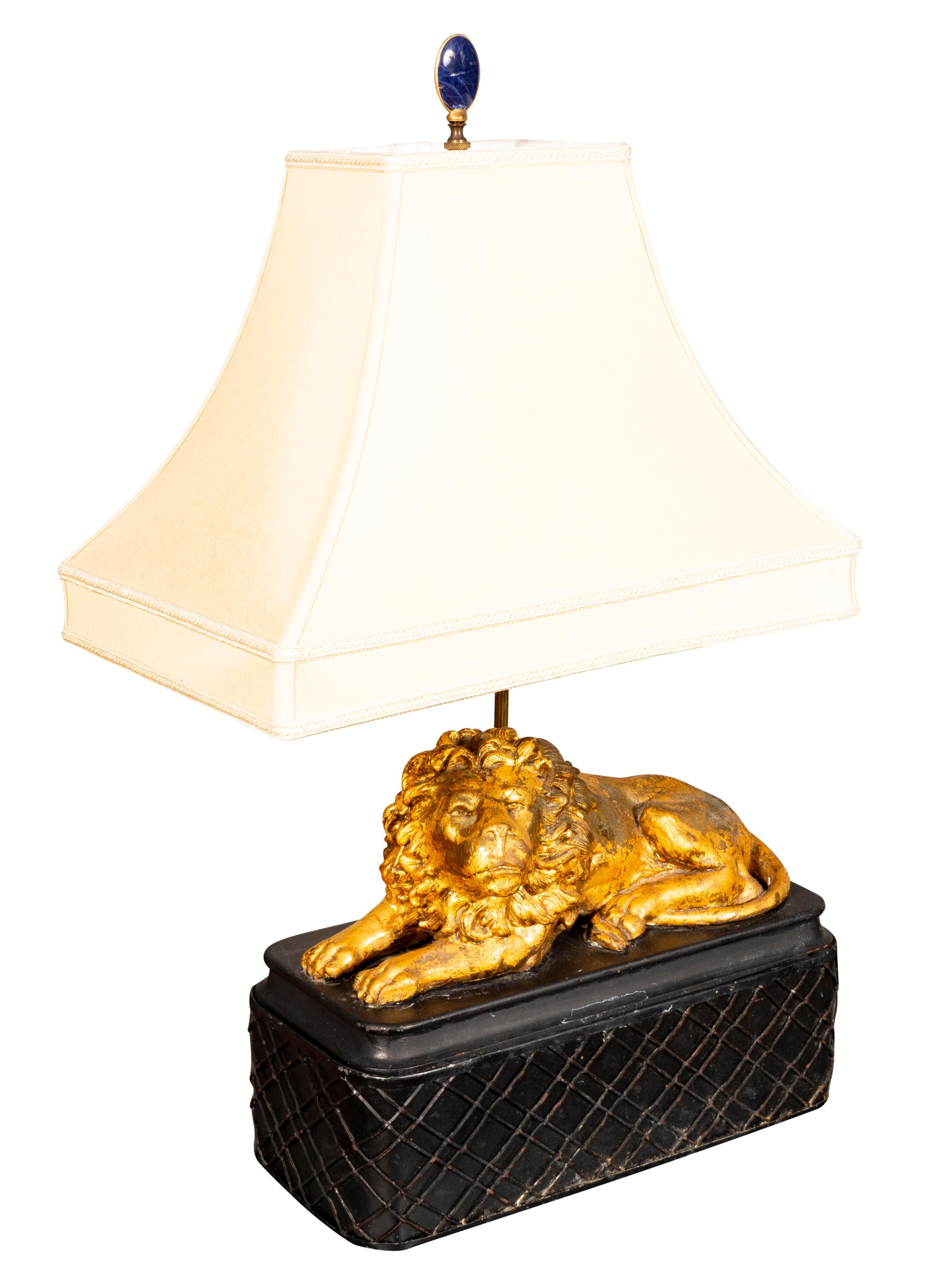 The lions are antique. Each seated on a rectangular ebonized base. With shades. Two light socket. The lions are early with lots of touchups to the gilding. They are carved wood and gesso and later with touchups. Lapis finials.
