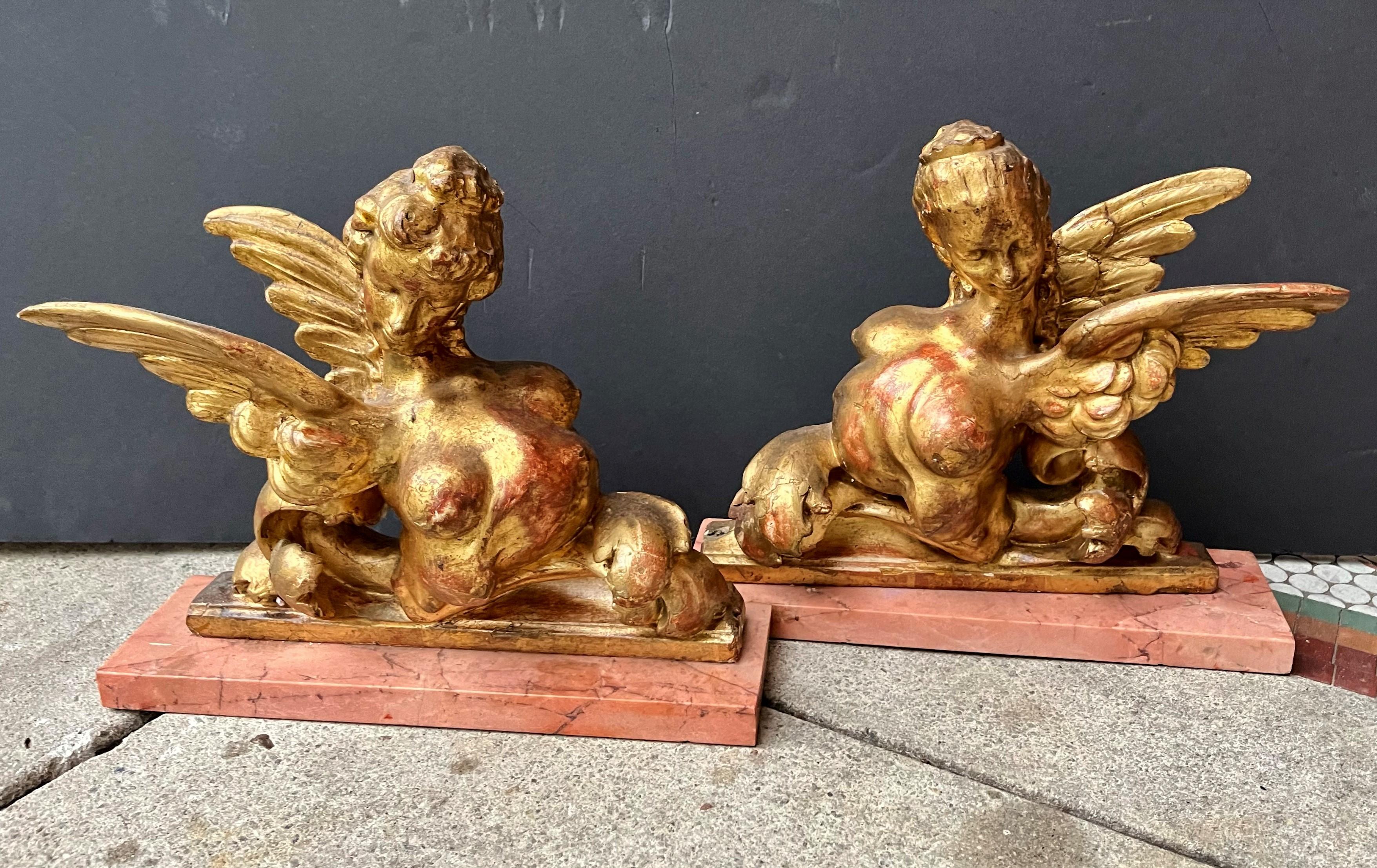Probably Mdme. Pompadour and Mdme. DuBarry caricatures, popular motif in the 19th century. On coral colored marble bases, and probably of architectural origin. Great color contrast between red bole and gilding.

Usual aging issues with giltwood,