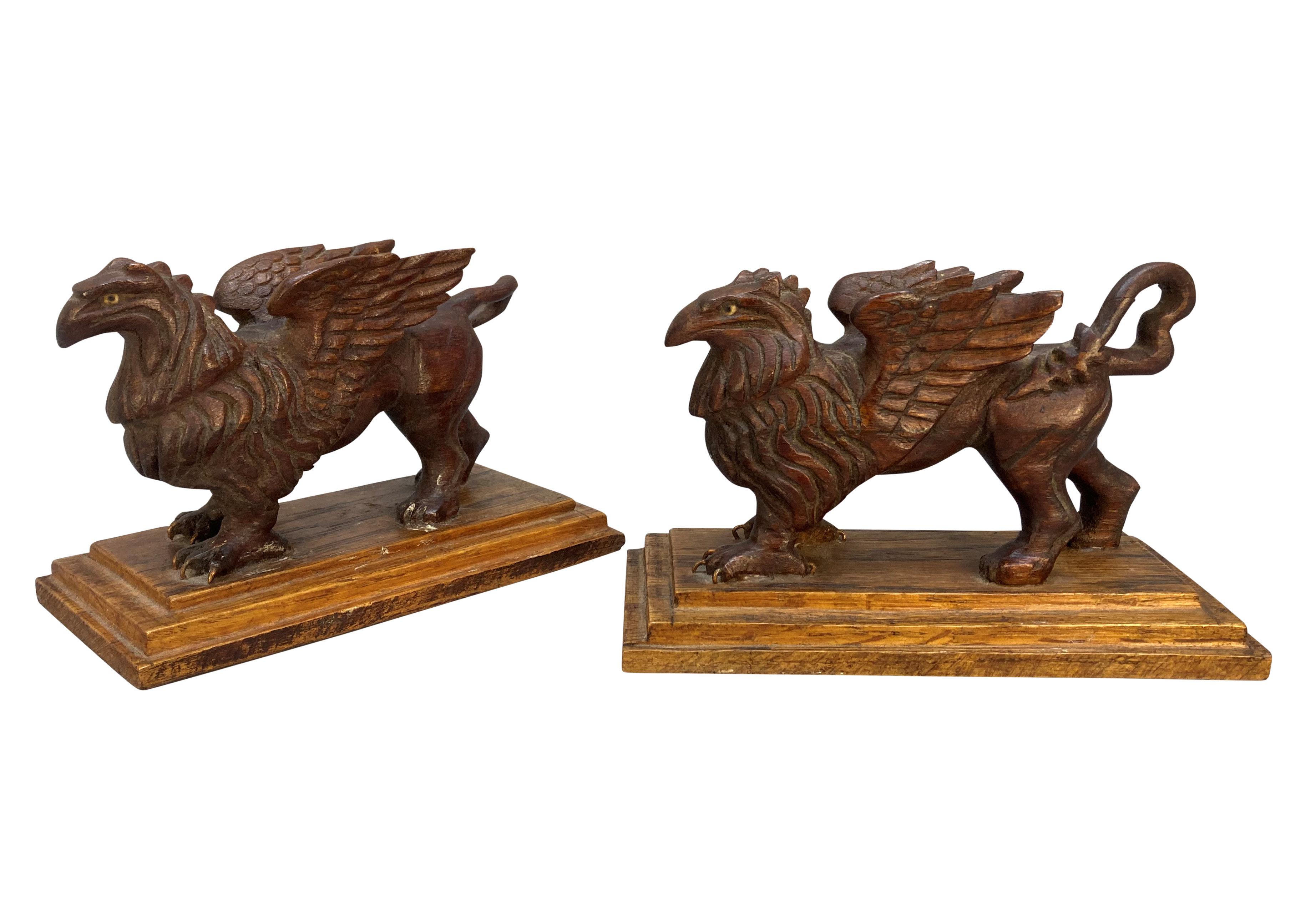A pair of English carved fruitwood griffins, on plinths.