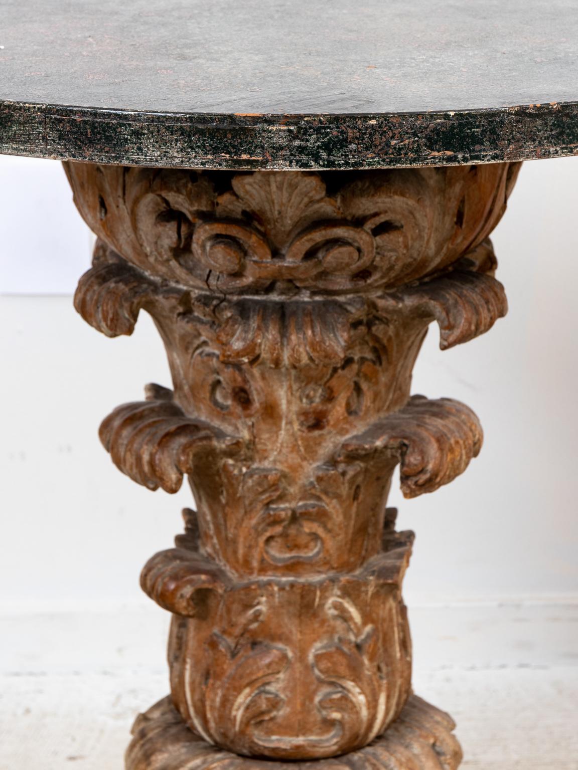 Circa 1900s pair of carved lime oak tables with faux marble painted top and base. The pieces are further detailed with a scrolled foliage motifs on the pedestal base. Please note of wear consistent with age. Available as each.