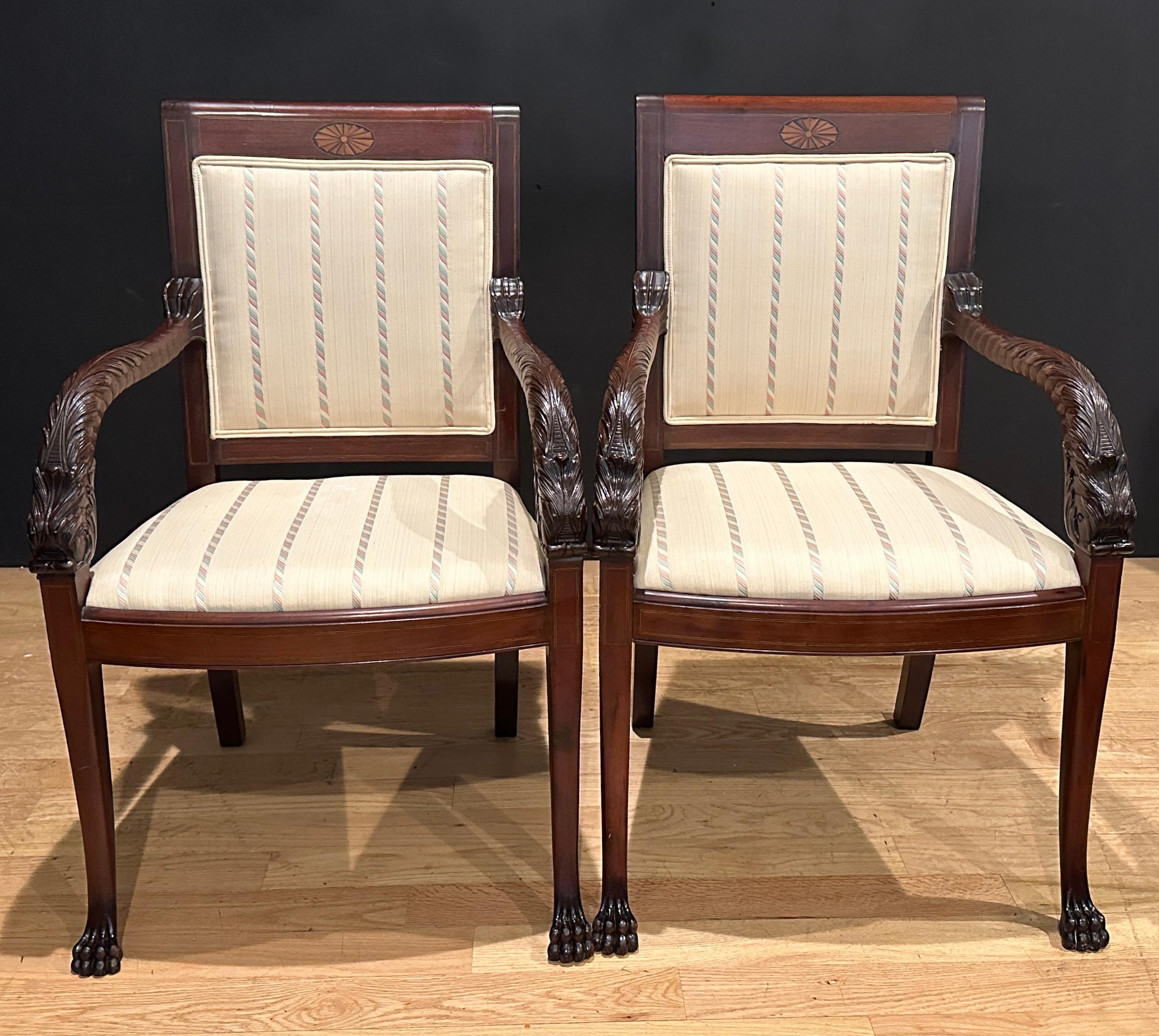 Pair of early 20th century hand carved mahogany armchairs with dolphin form arms. Fan design satinwood inlay on top rails. Square tapered legs with satinwood lay terminating in carved lion form feet.