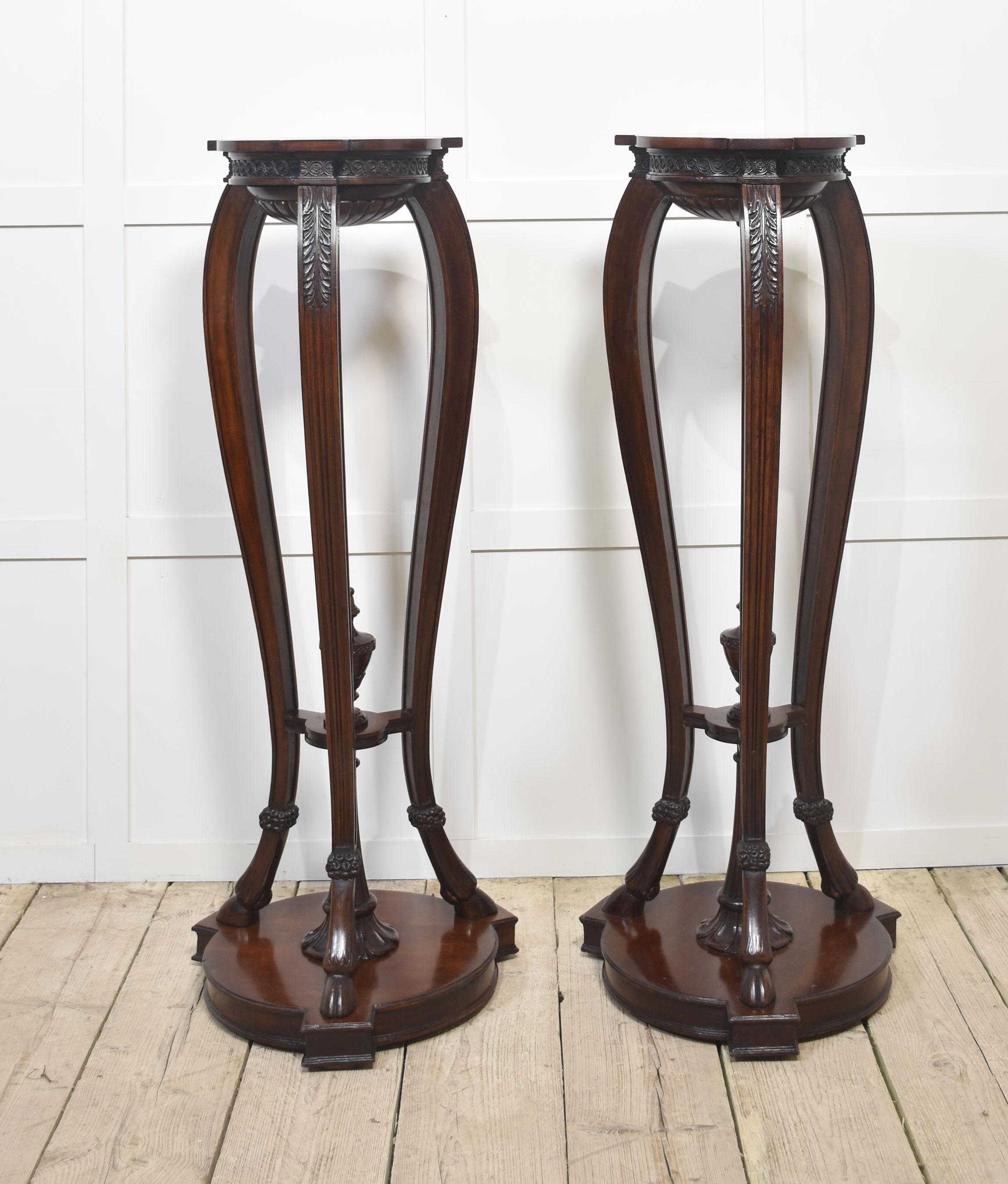Pair of Neo classical style carved mahogany torcheres the shaped tops and carved frieze with guilloche and acanthus leaves detail. To the shaped legs united by under-tier with central urn. All raised up on Hoof feet and moulded