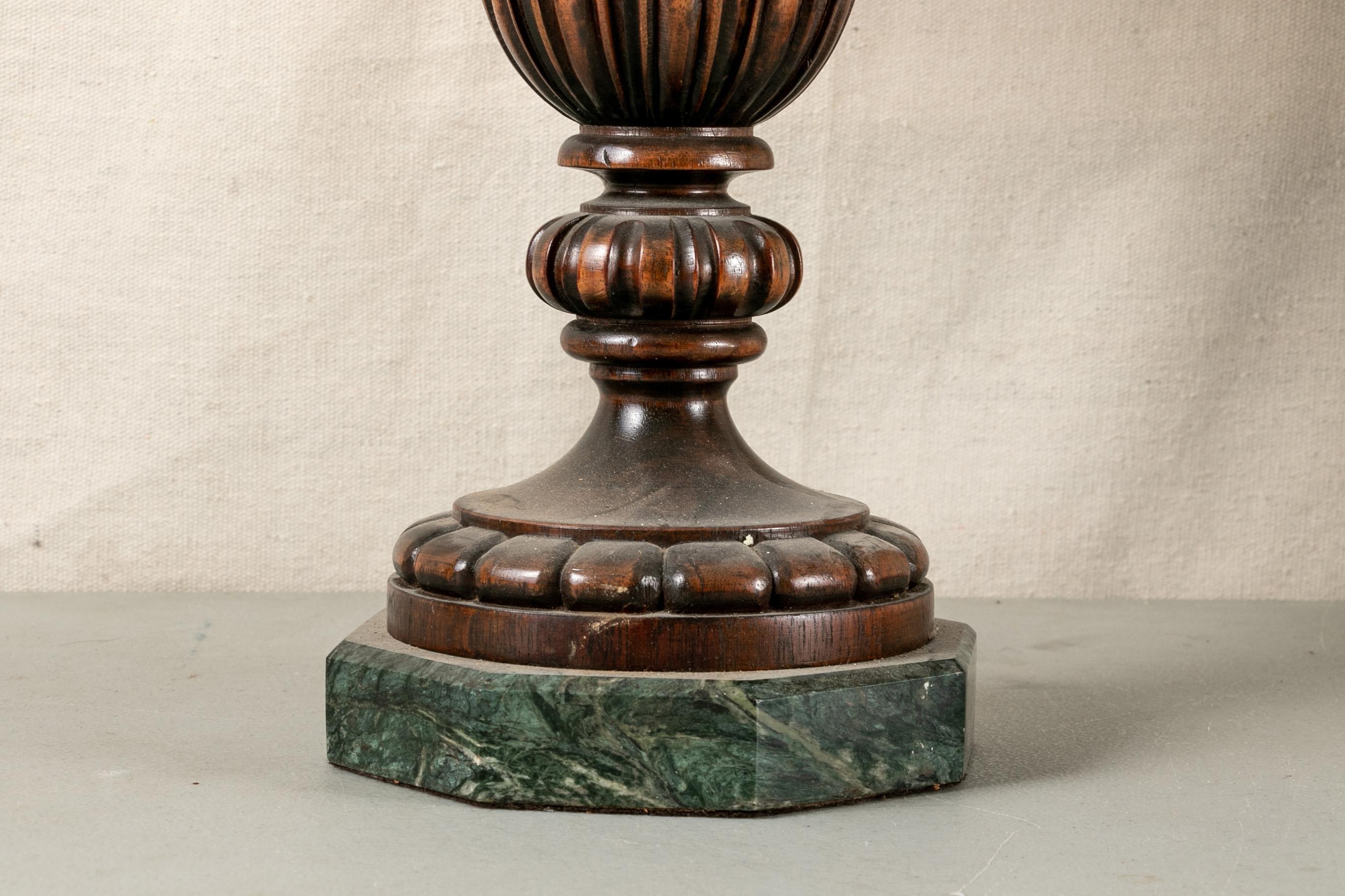 Pair of carved mahogany table lamps, three light fluted urn form lamps with turned tops and flared bases. Mounted on octagonal green marble bases. With a fine old patina. Green on ecru leafy printed and pleated shades. 

Condition: Expected wear