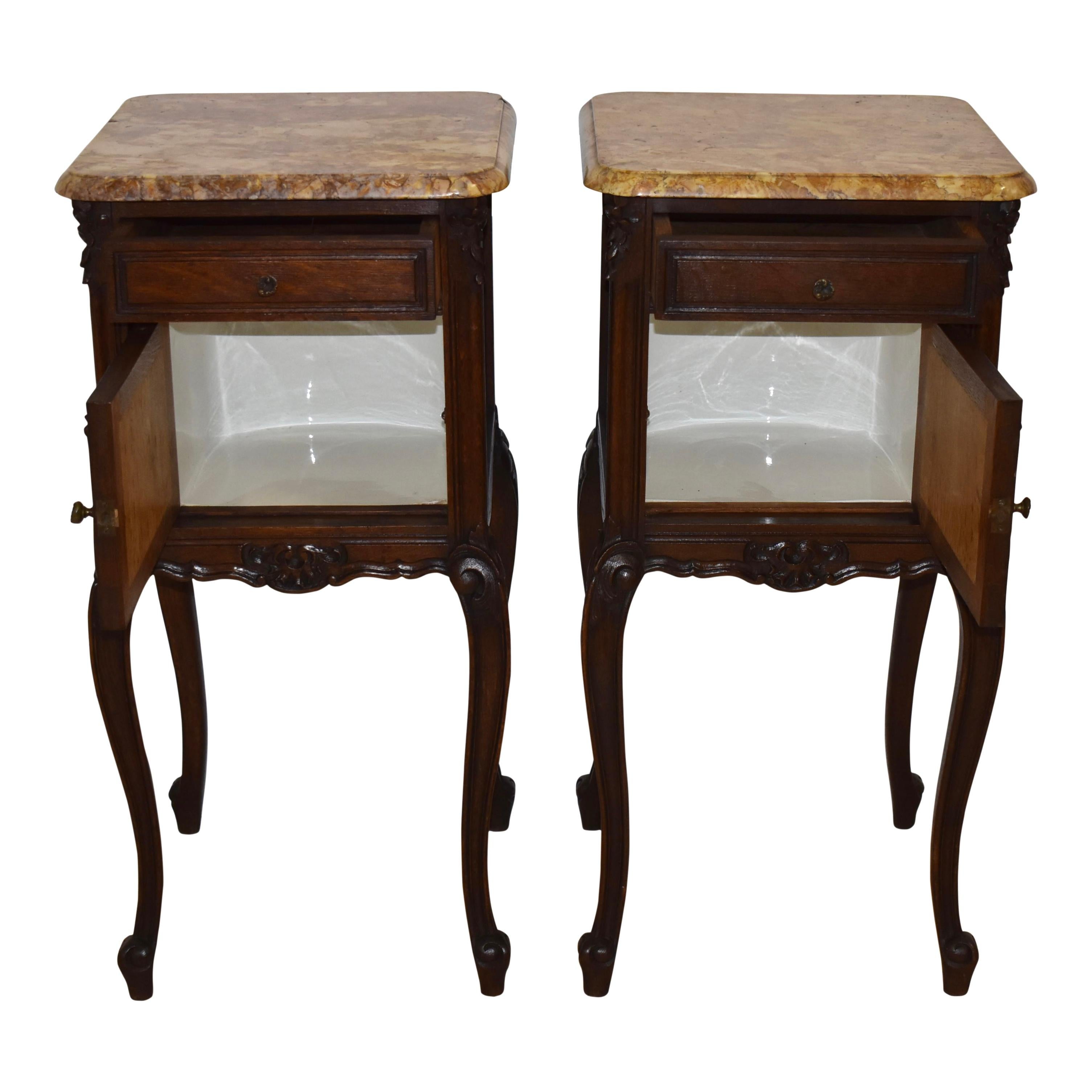 This beautiful set of nightstands pairs oak frames finished with a rich, dark stain and marble tops, showcasing gold, cream, and tan tones. The nightstands date back to the years when a bedside table's purpose was to provided storage for a chamber