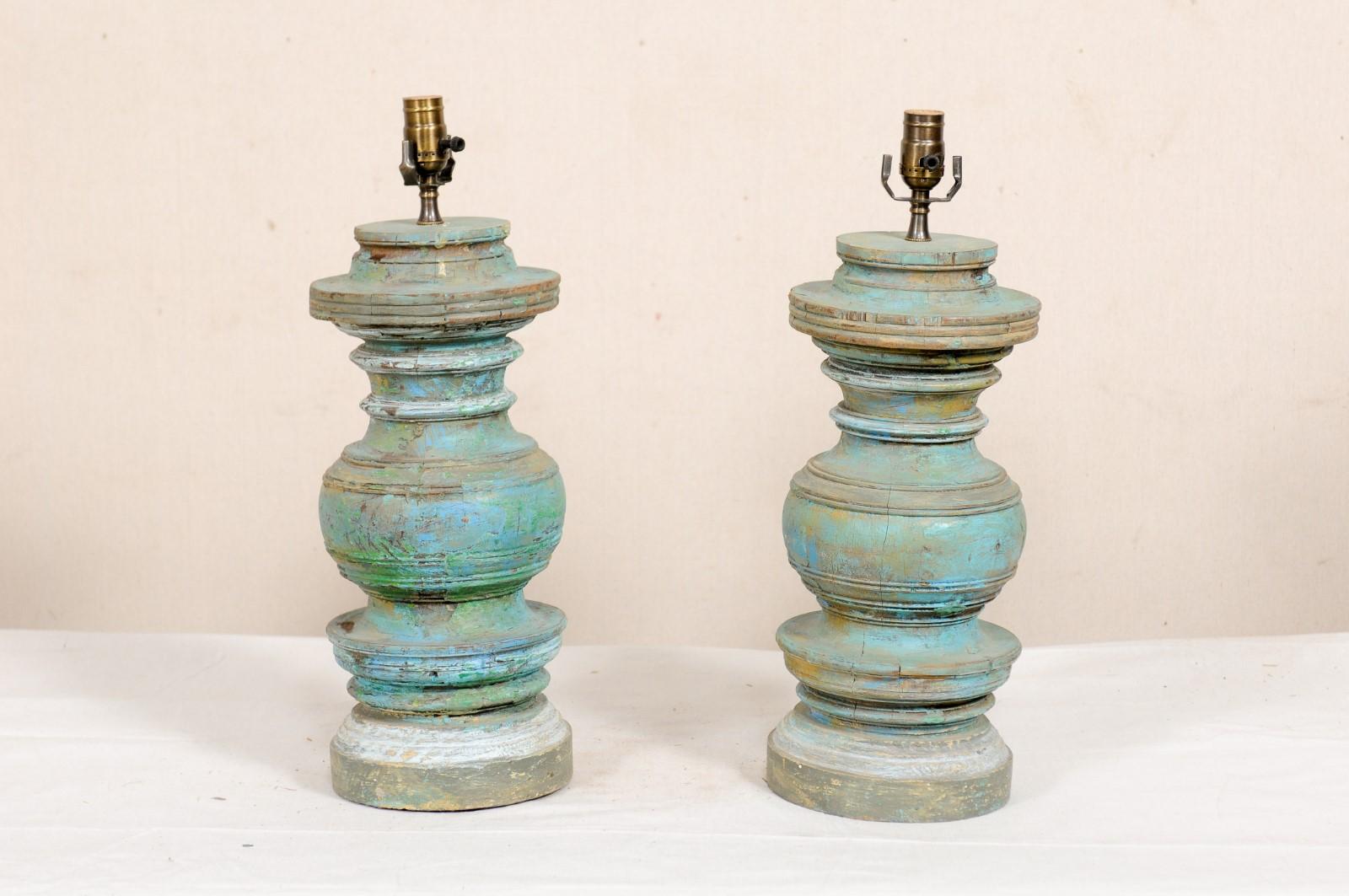 A pair of painted and nicely turned table lamps fashioned out of old wood columns. This pair of lamps feature a thick central column, heavily carved with concentric circular rings and trim about the exterior, and raised on a stacked and rounded