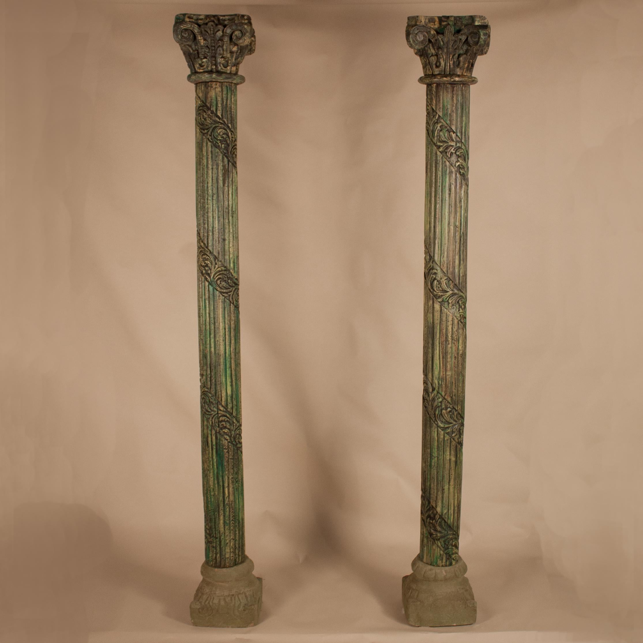 Distinctive set of teak wood columns from Gujarat, India, circa 1950, with original green paint and hand-carved, ribboned flutes and Corinthian capitals. The column bases, which have a small footprint, are made of sandstone and have weathered, yet