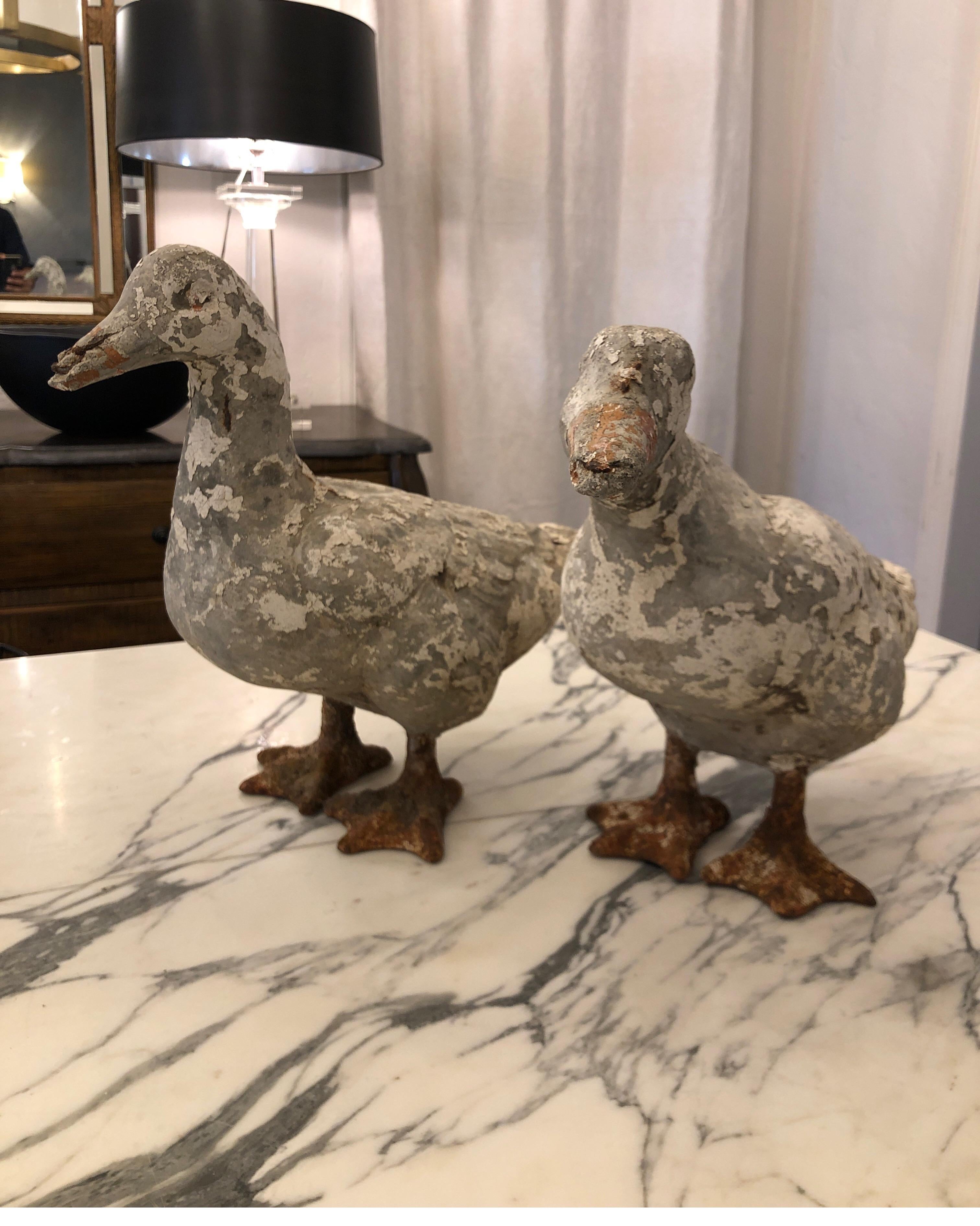 Life-size pair of carved stone duck sculptures with iron webbed feet.
One depicts a duck standing with his neck stretched out and the other is in a natural standing position. Both are weathered with unique patina and rusty hues on the webbed