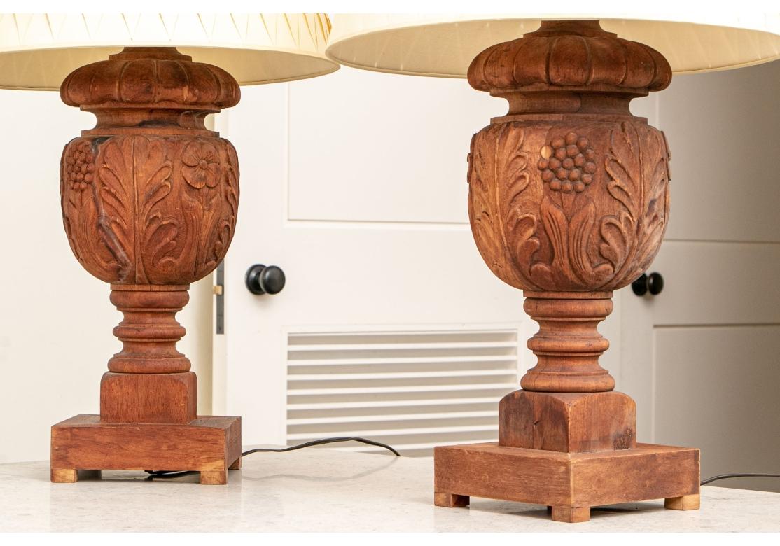 A unusual, decorative and artistic pair of carved wood lamps. Carved urn form standards with floral and foliate motif, square footed base. Covered with a woven paper shade and brass ball finial.

Dimensions: 31 1/2