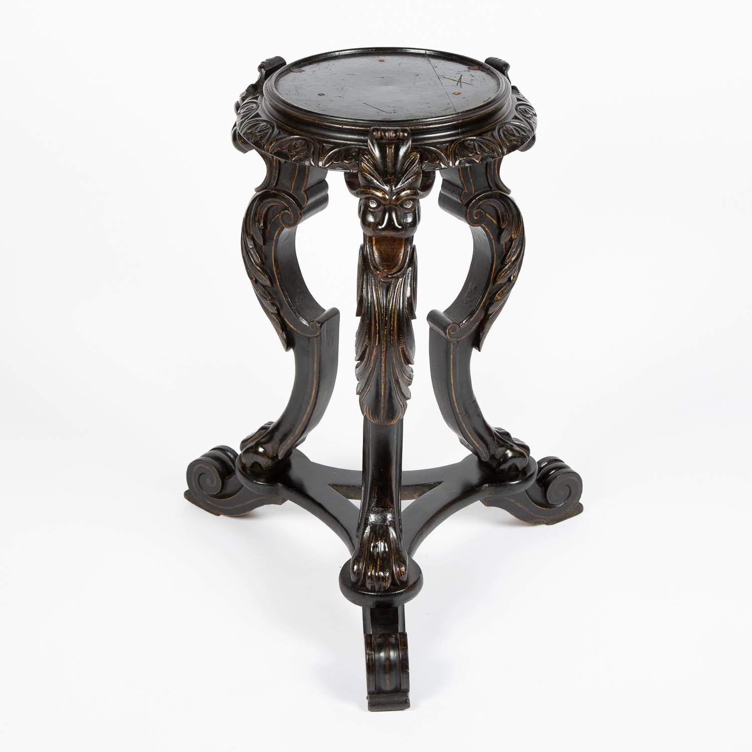 A pair of late 19th century ebonized tripod vase stands, carved with Griffins heads and floral motifs, retaining faint gilt highlights. English, circa 1880.