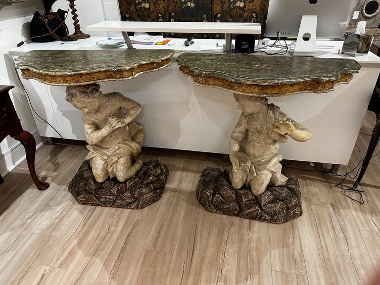 A fine pair of carved and gessoed 18th C. Venetian console tables with demilune shaped faux marble tops, resting on large, intricately carved mirrored putti, kneeling on carved and painted faux stone bases. Acquired from the Belair, California,