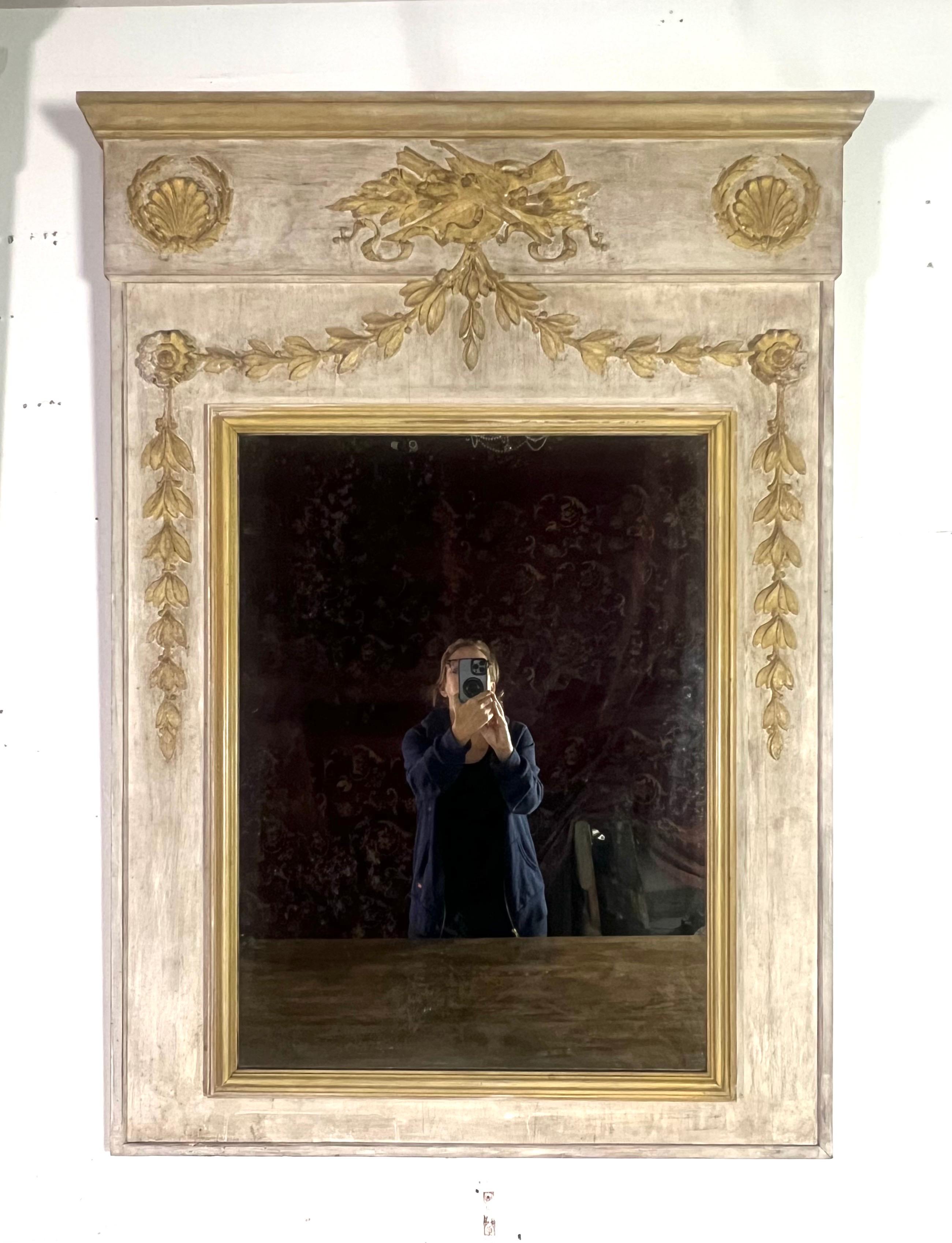 Coppia di specchi rettangolari in stile neoclassico.  Gli specchi sono dipinti in color crema, con dettagli dorati.  La parte superiore di ogni cornice comprende un frontone decorativo, con un intaglio centrale in rilievo di uno strumento musicale e