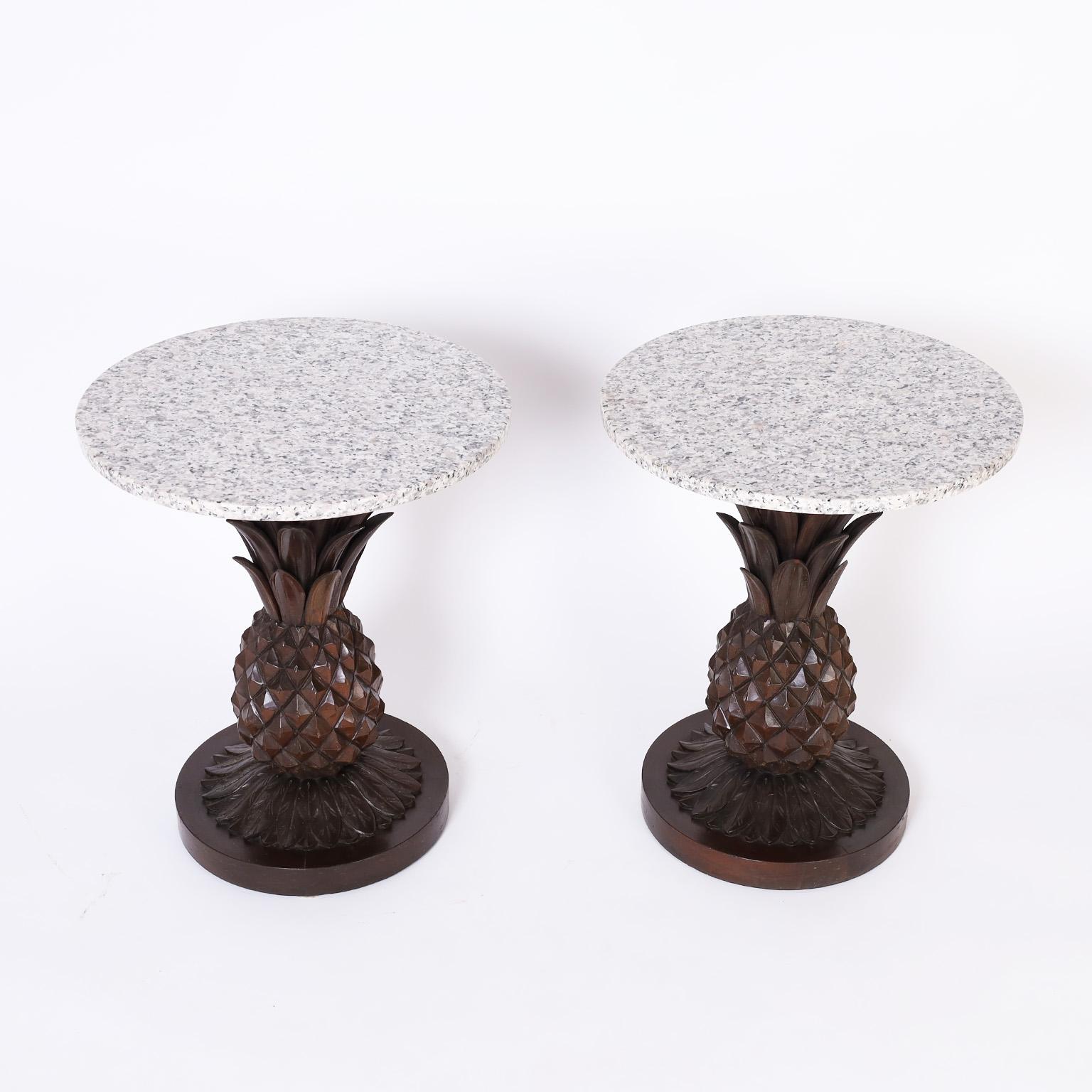 Mid century round marble top stands featuring conspicuous carved mahogany stylized pineapples over leaves on round wood bases.