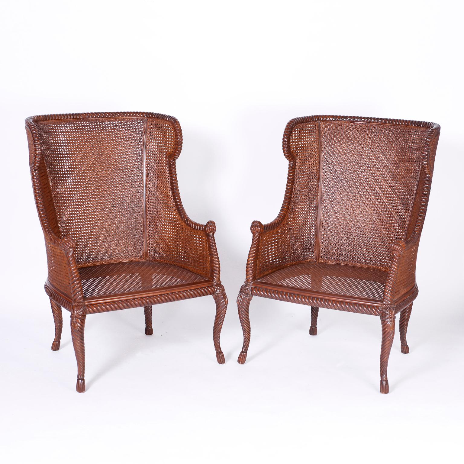 Pair of wingback armchairs featuring carved mahogany frames with a rope and tassel motif, double caned backs, sides and seats, cabriole legs with tassel feet and an overall elegant form.

Measure: Seat height: 20